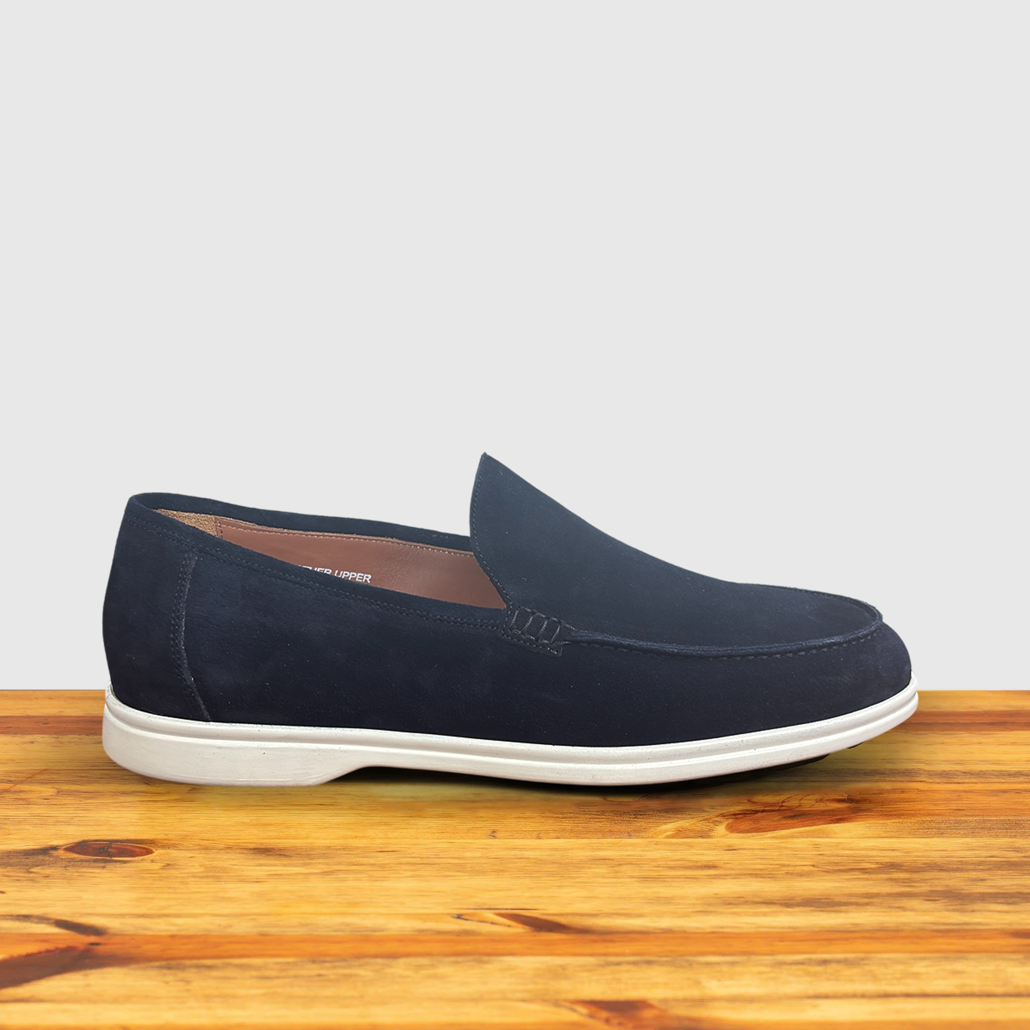 A Navy Blue suede loafer with white sole, displayed on a wooden surface.