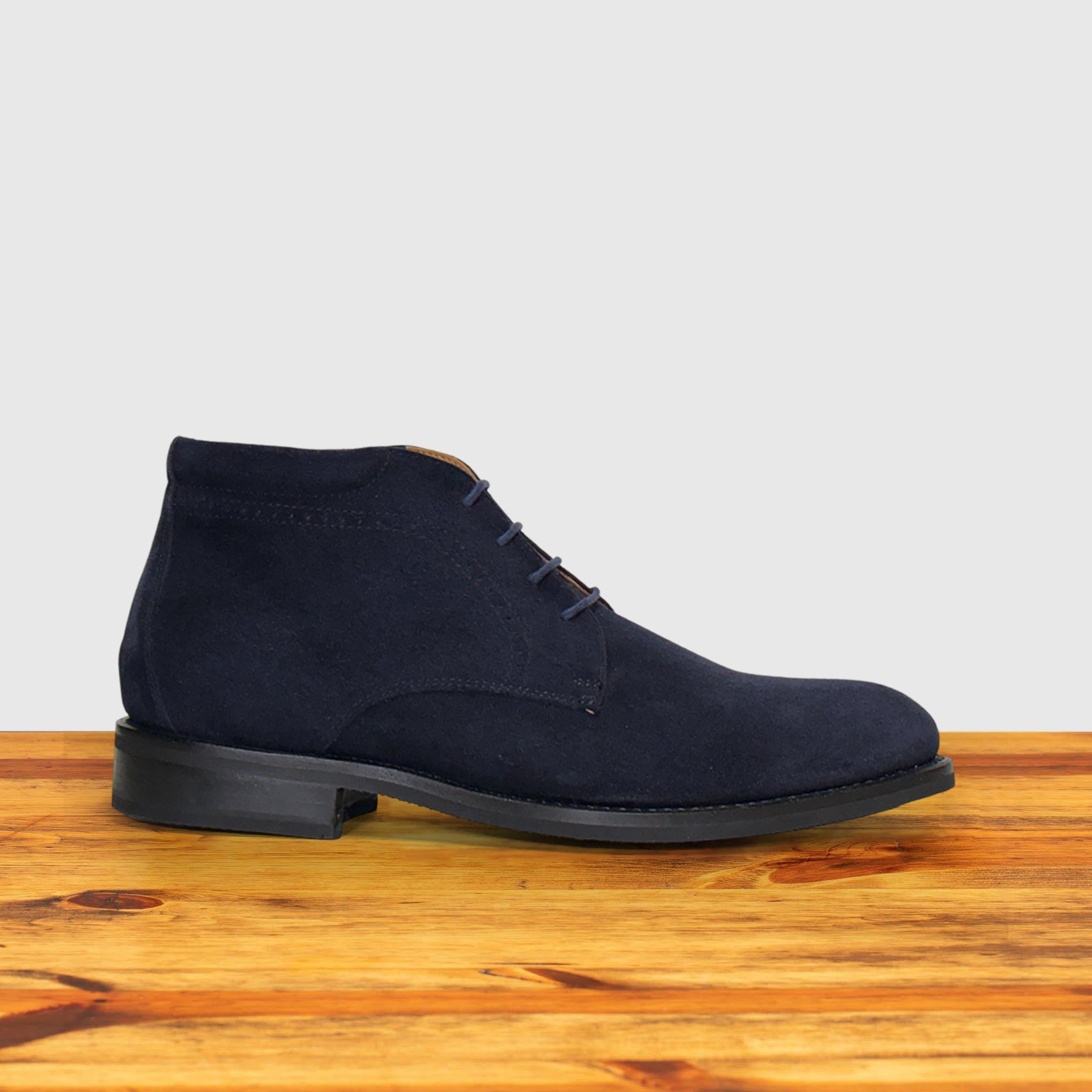 Navy blue suede shoes on a wooden surface with a light gray background