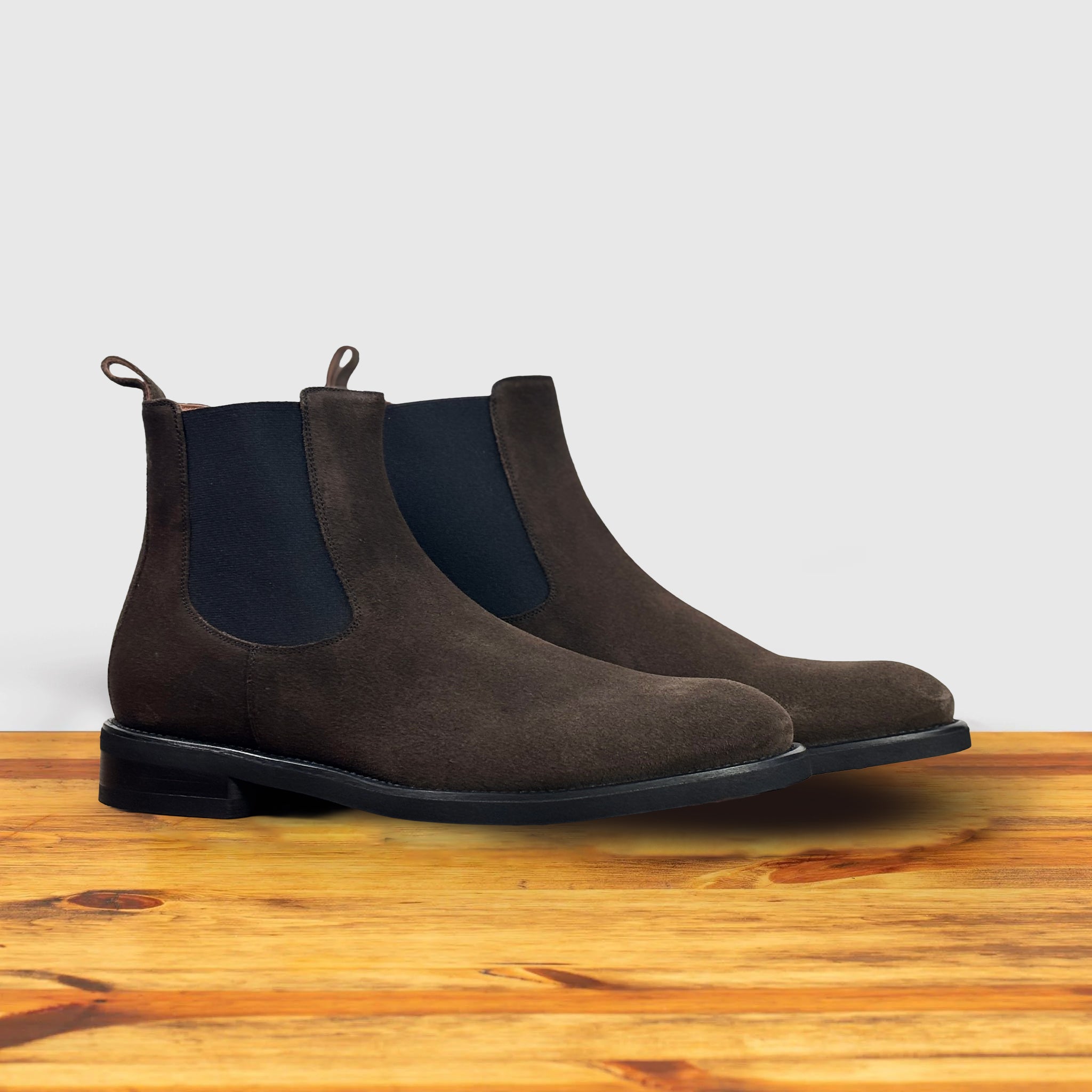 Brown suede Chelsea boot on a wooden surface with a light gray background