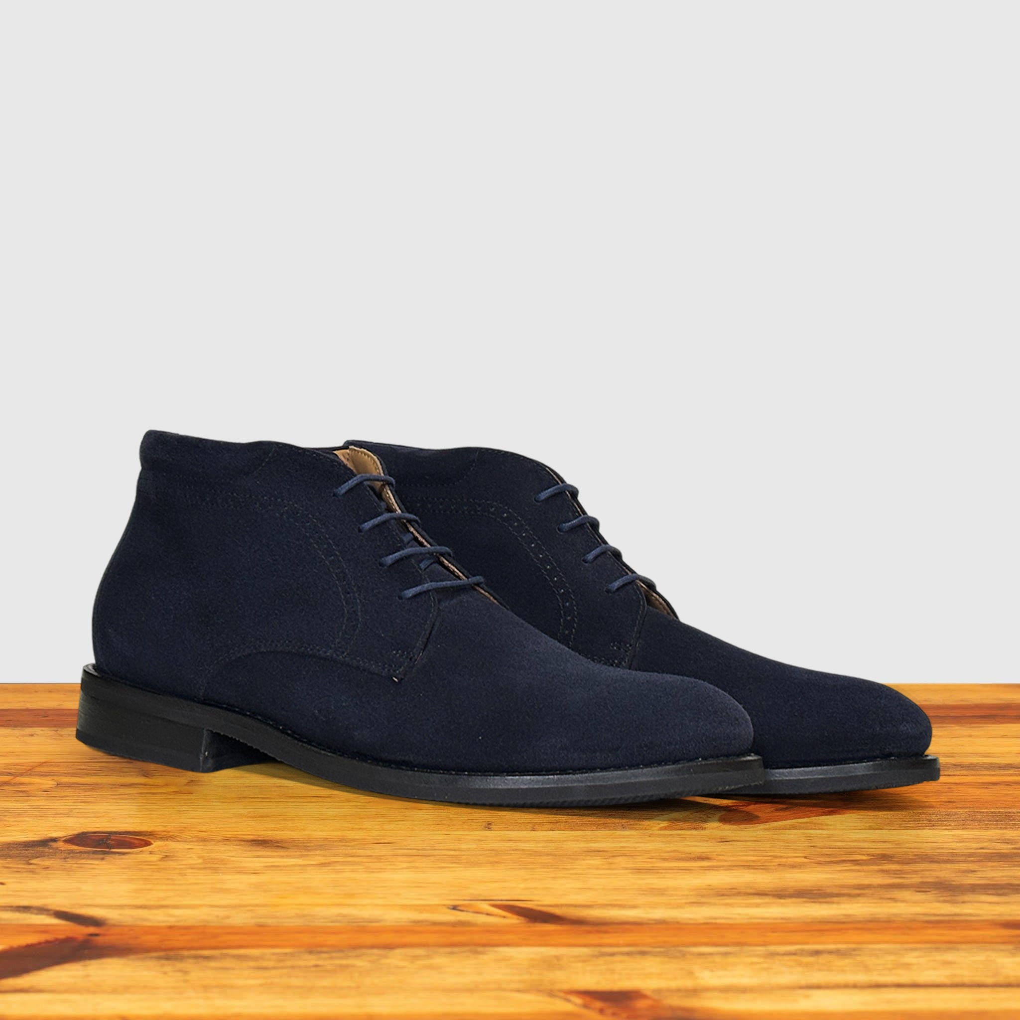 Pair of Navy blue suede shoes on a wooden surface with a light gray background