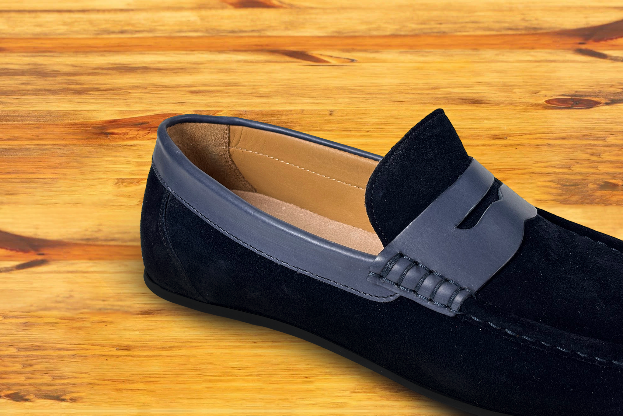 A navy blue suede penny loafer with a strap, displayed on a wooden surface.
