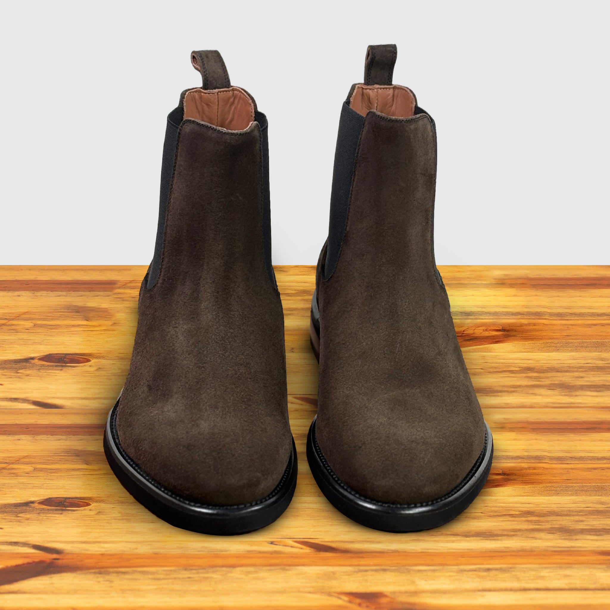 Brown suede Chelsea boot on a wooden surface with a light gray background