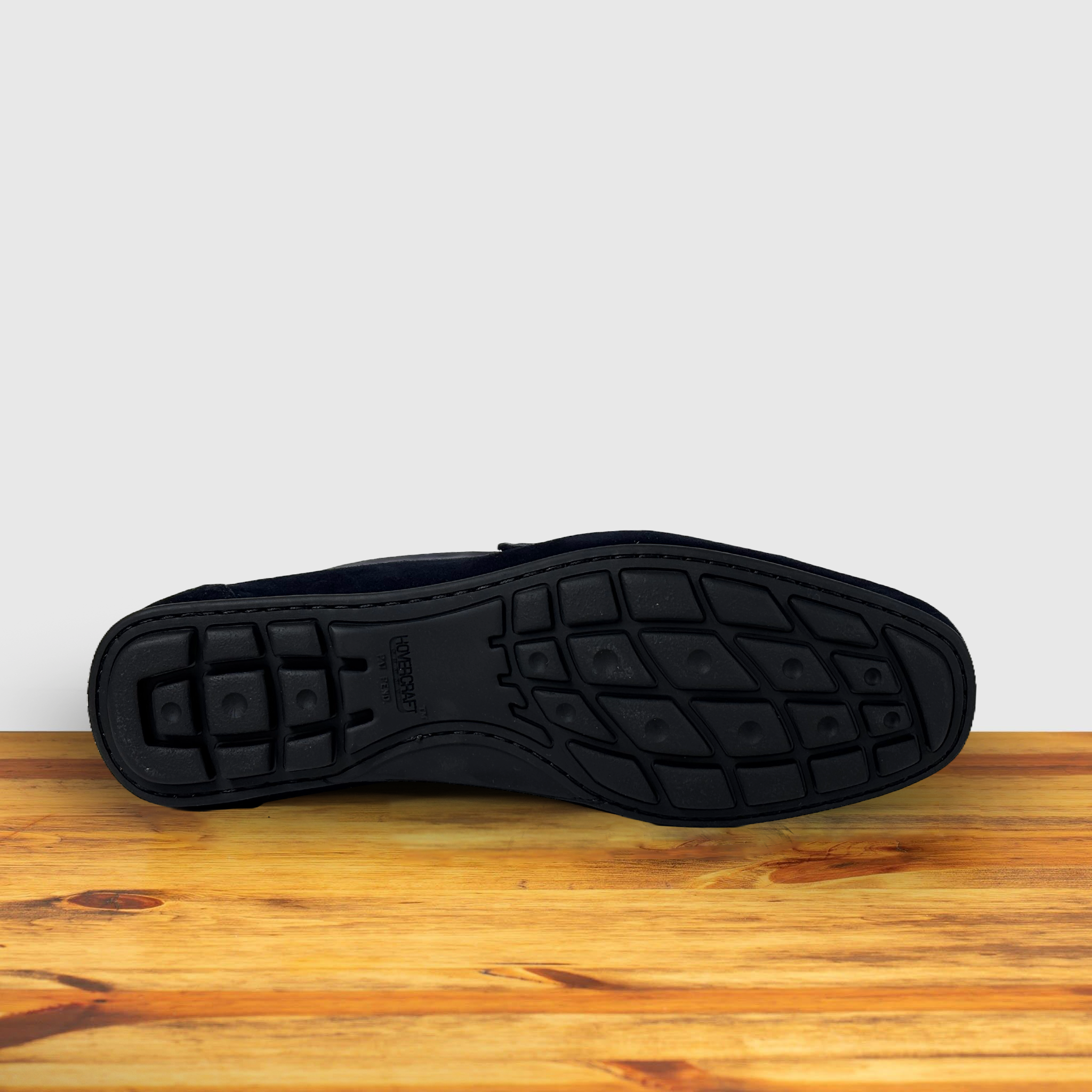 Back of a navy blue suede penny loafer with a strap, displayed on a wooden surface.