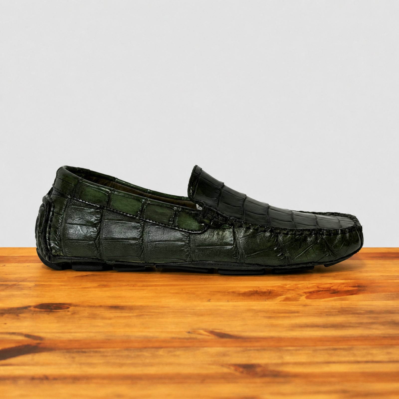 Green genuine crocodile leather loafer on a wooden surface with a light gray background