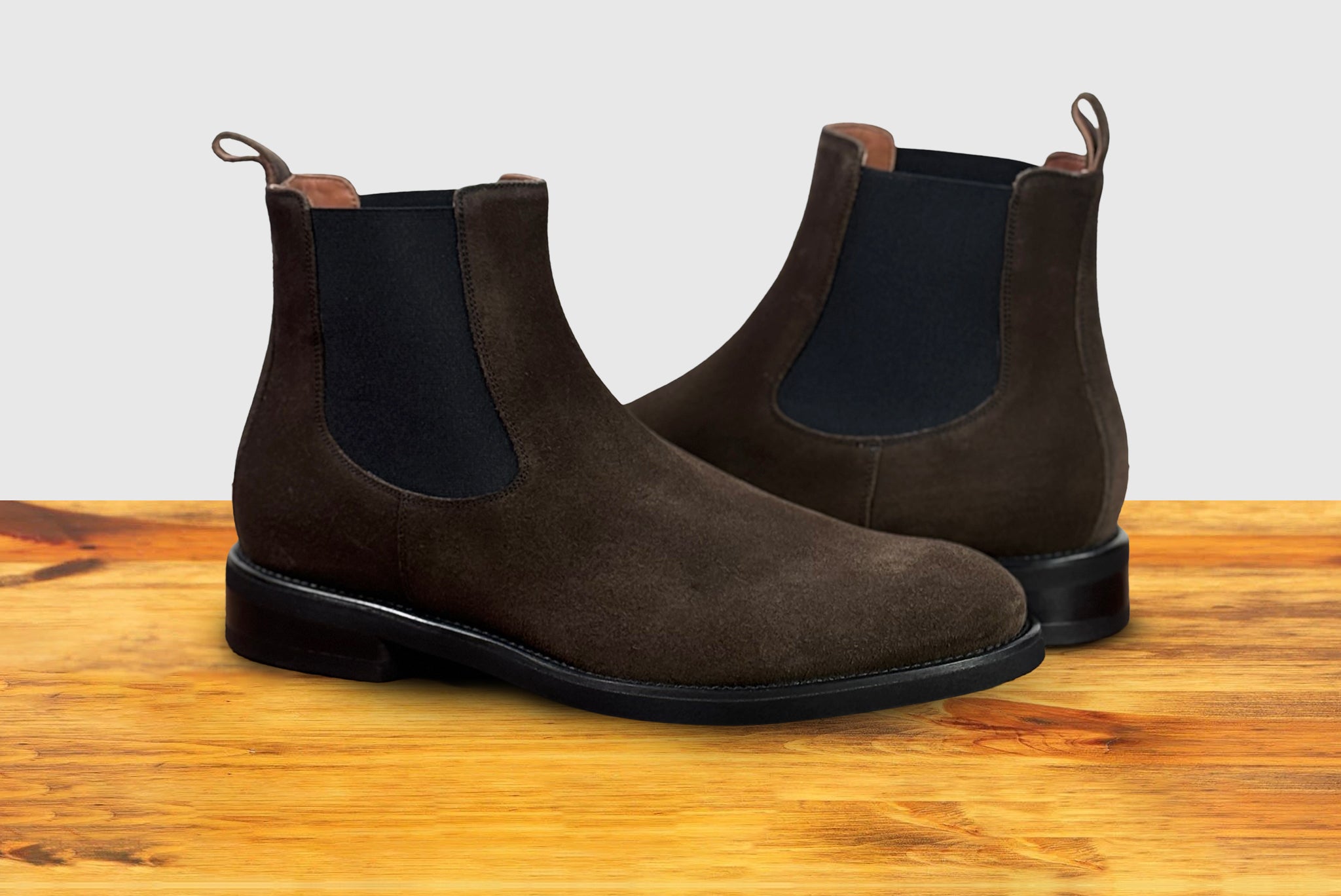 Brown suede Chelsea boot on a wooden surface with a light gray background