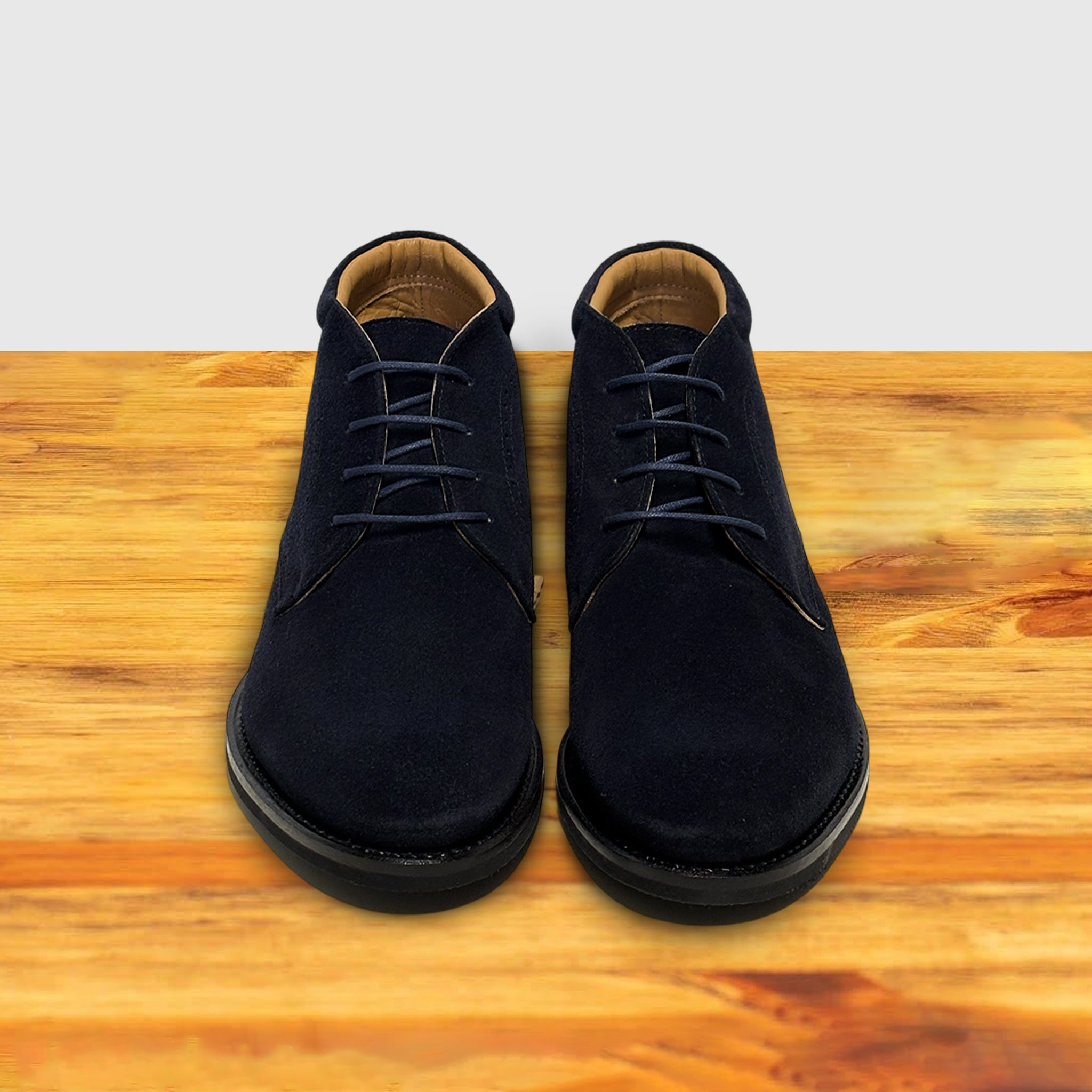 Pair of Navy blue suede shoes on a wooden surface with a light gray background