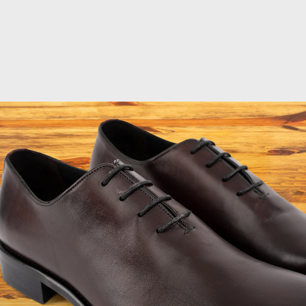 Close view of burgundy Italian wholecut Oxford shoe with laces on a wooden surface.