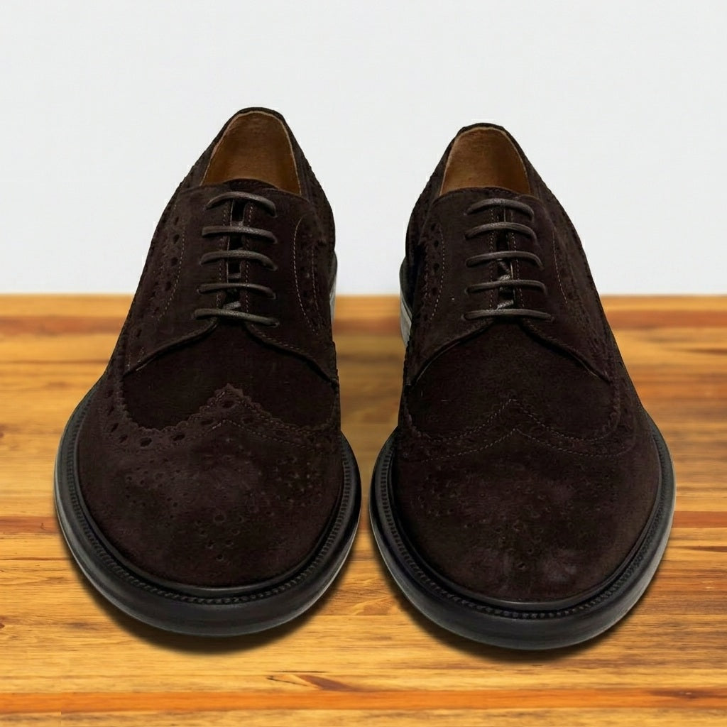 Pair of Chocolate brown suede wingtip shoe with decorative perforations and lace-up closure, displayed on a wooden surface