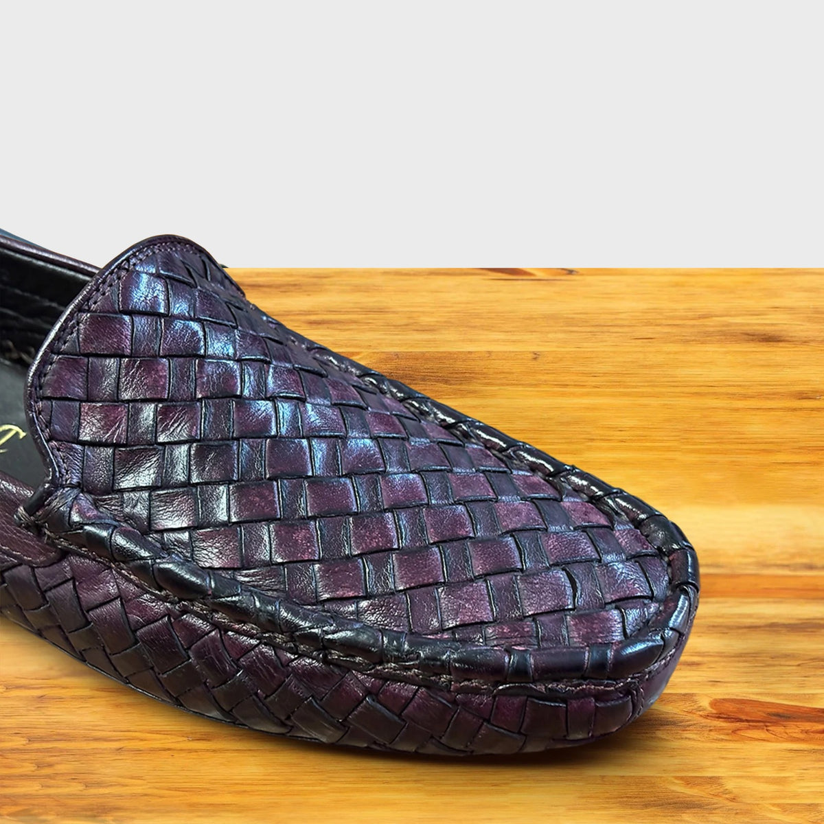 Close view of Merlot loafer shoe with woven pattern on a wooden surface