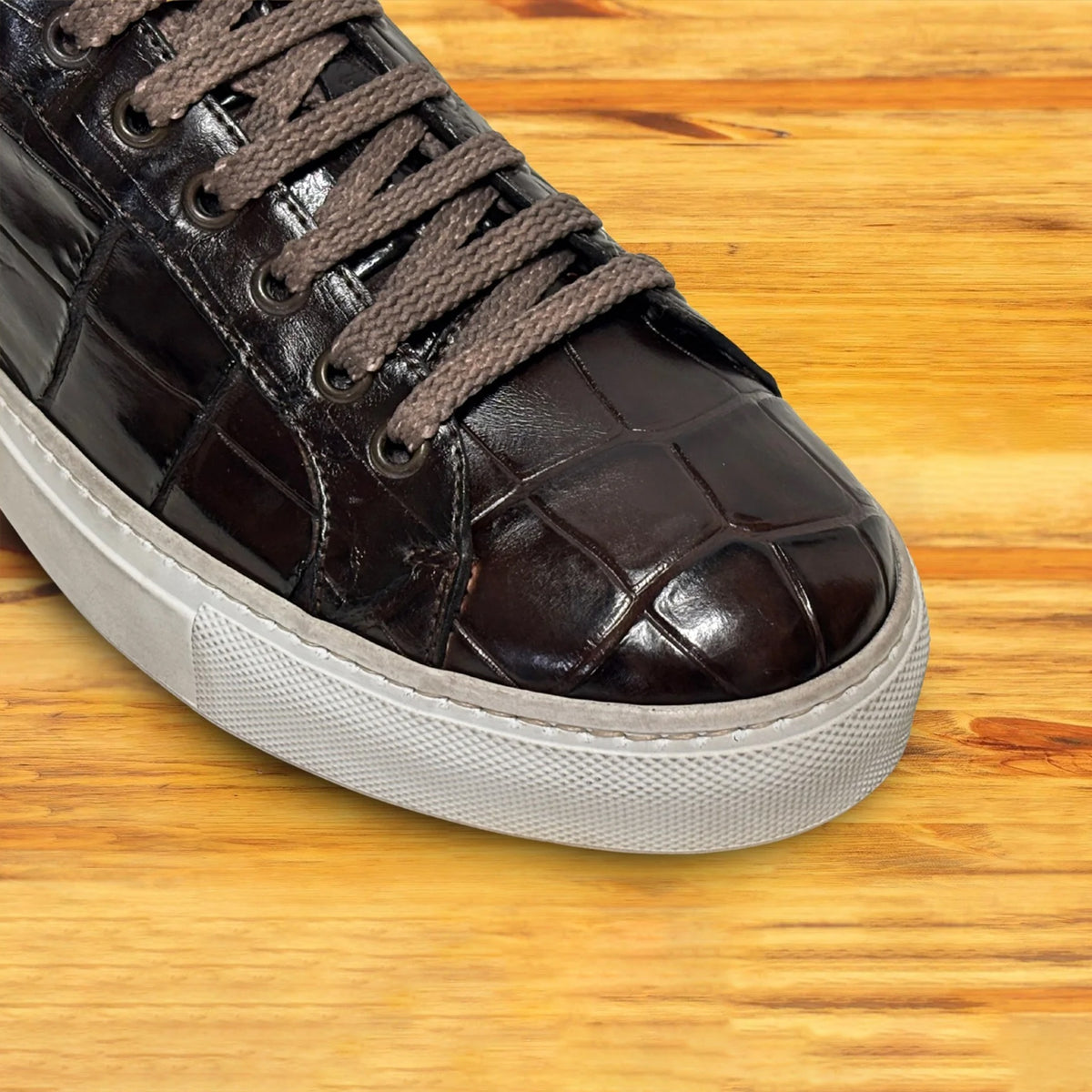 Close view of Dark Brown sneakers with white soles on a wooden surface