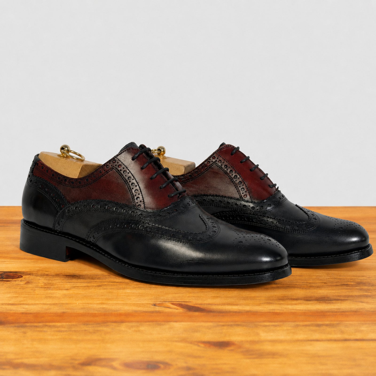 A pair of men's blue and Bordeaux oxford shoes with black laces, displayed on a wooden surface against a light gray background.