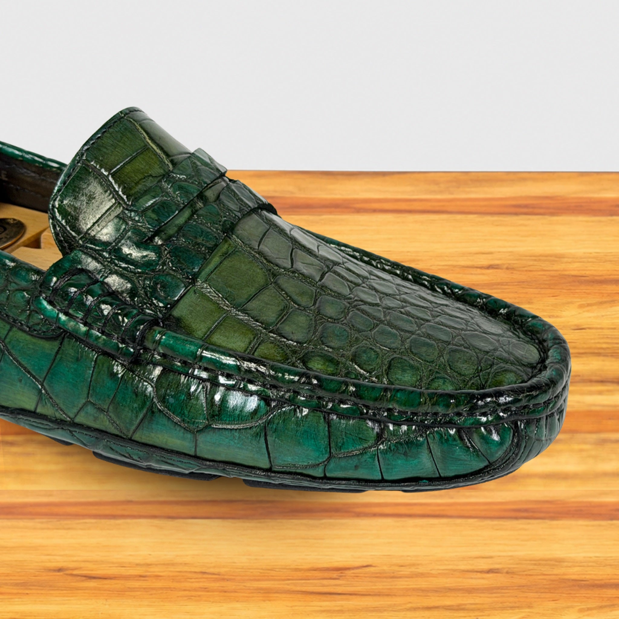 A single Emerald Green crocodile-embossed loafer shoe resting on a light brown wooden surface against a white background.