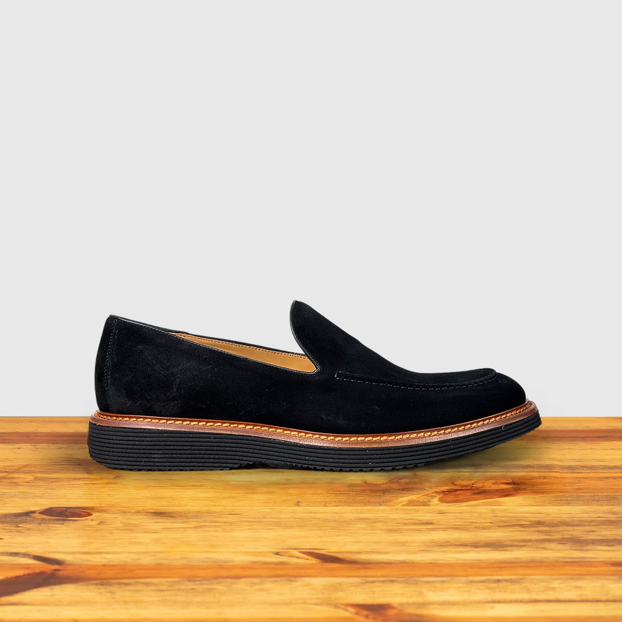 Black Venetian loafer with a rubber sole positioned on a wooden surface.