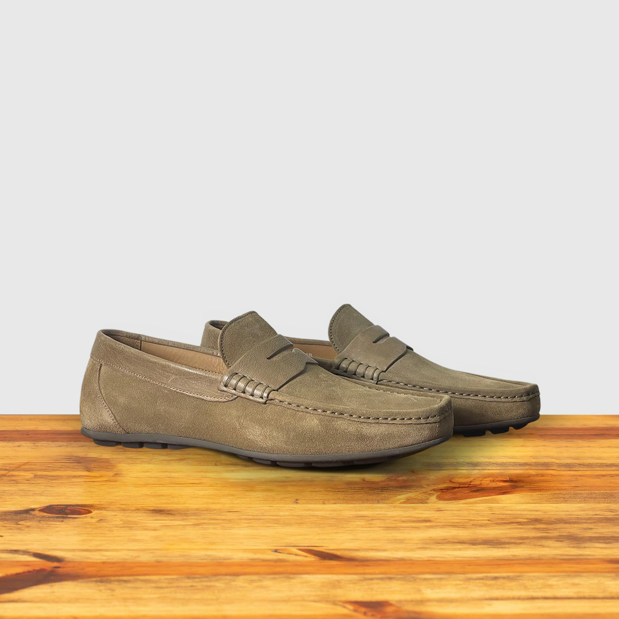 A pair of Rope color suede penny loafer, displayed on a wooden surface.