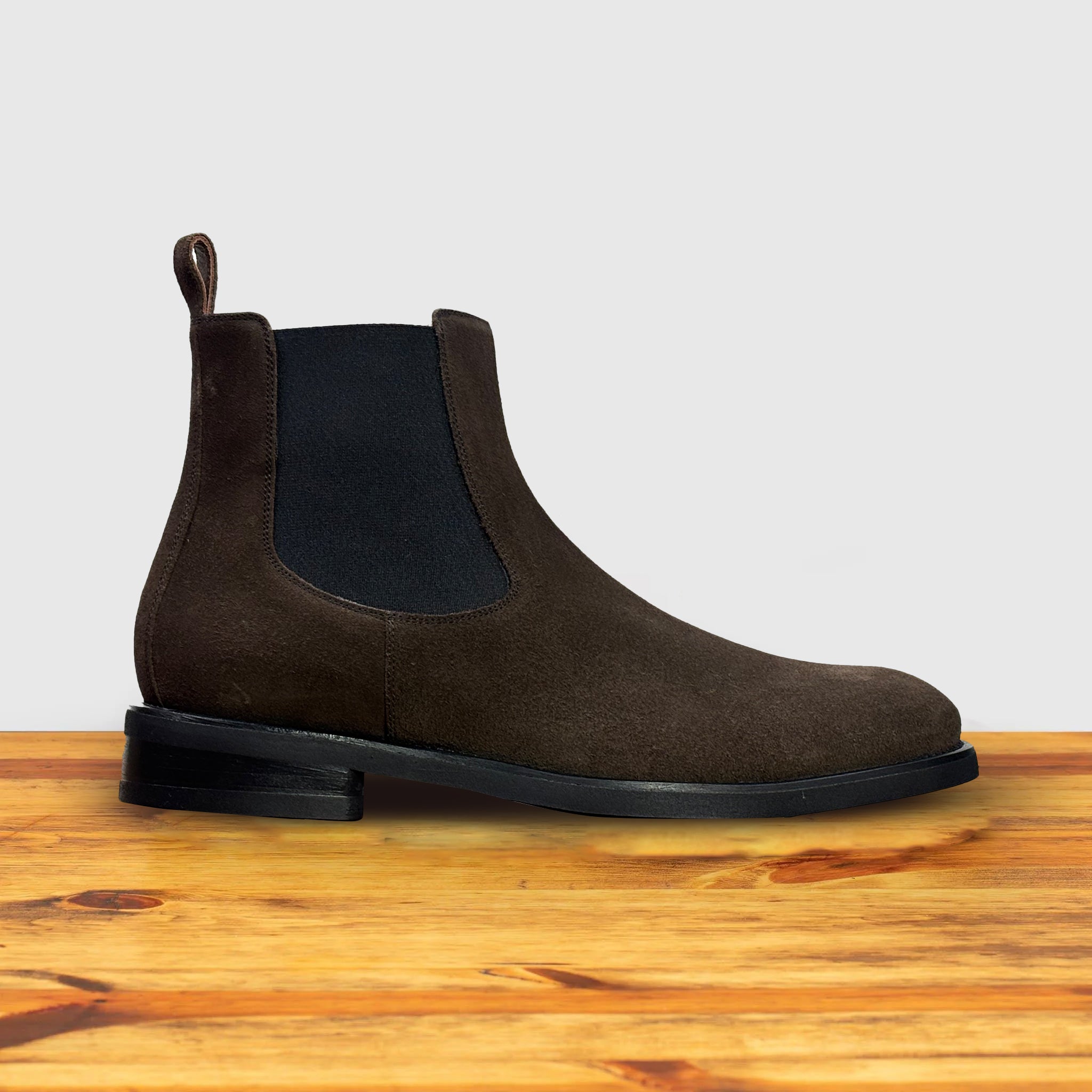 Brown suede Chelsea boot on a wooden surface with a light gray background