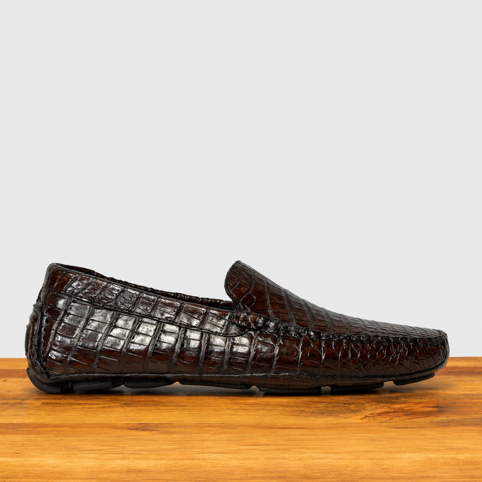 A single cerris color crocodile leather loafer shown in profile on a wooden surface against a light gray background.