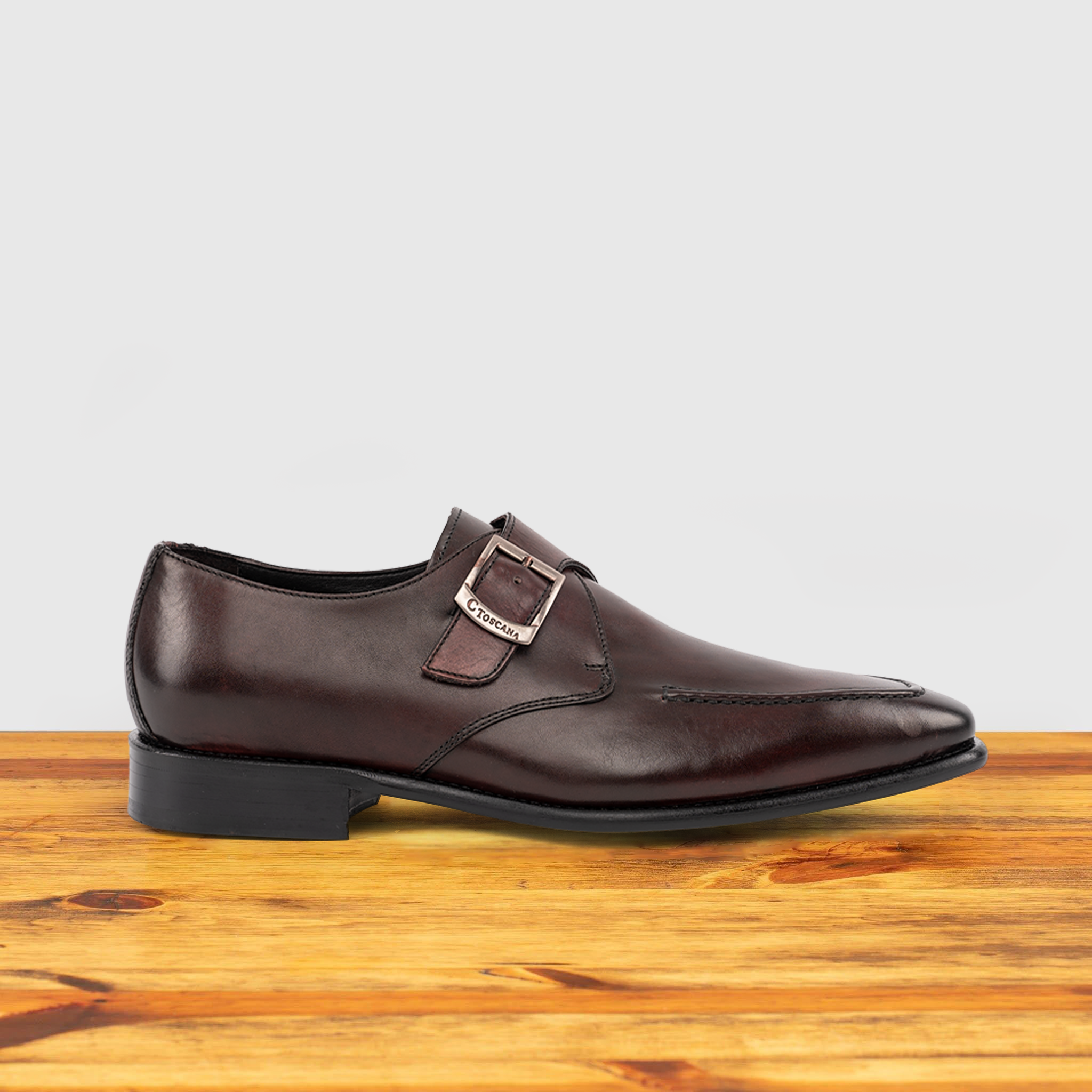 A burgundy monk strap shoe with a silver buckle on a wooden surface