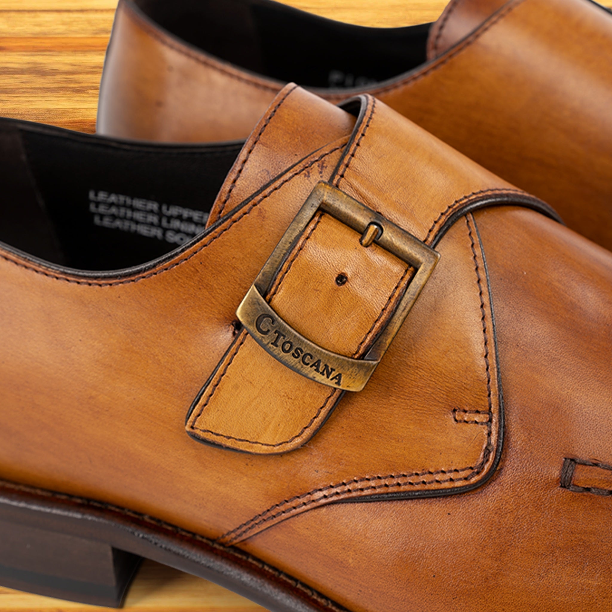 Brown leather shoe with a buckle detail on a wooden surface