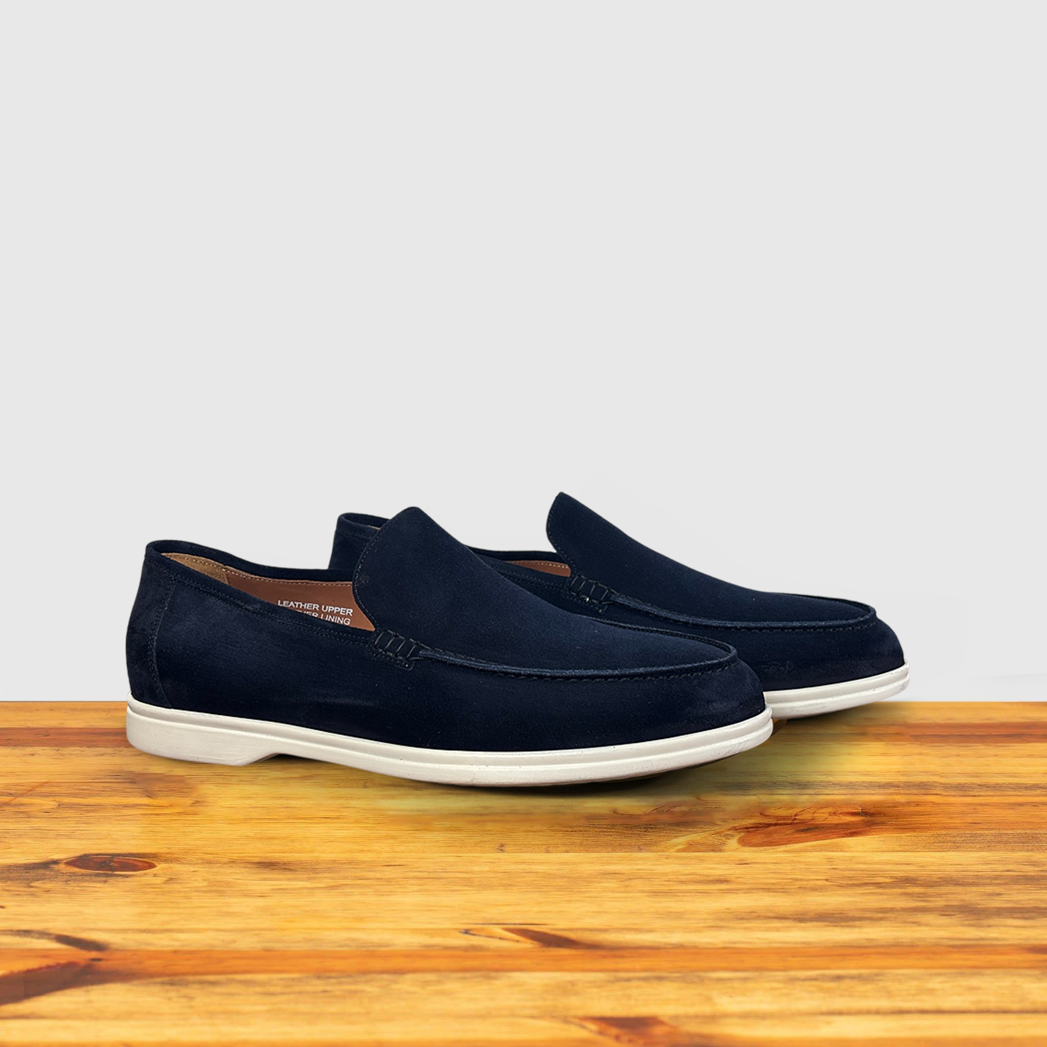 A Navy Blue suede loafer with white sole, displayed on a wooden surface.
