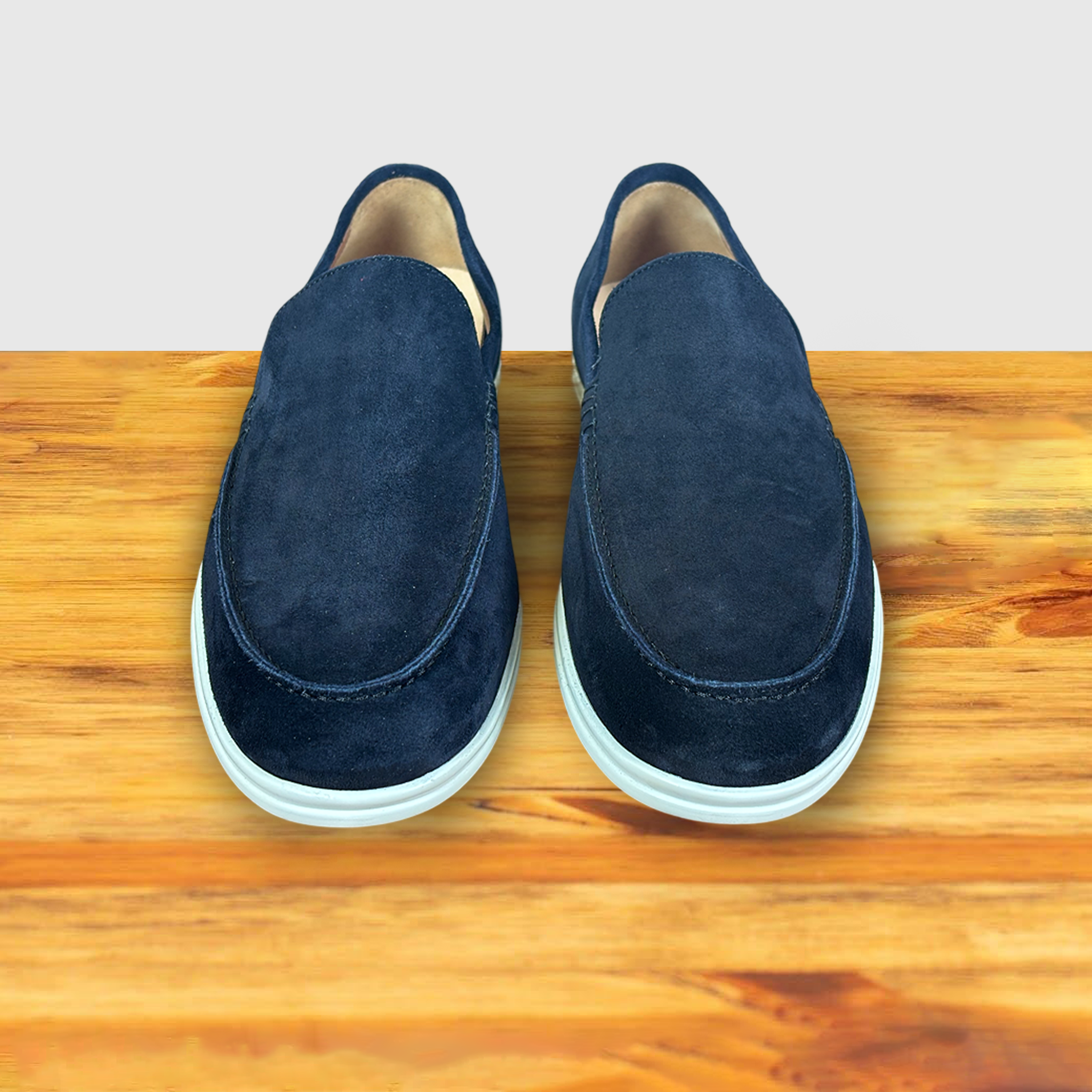 A Pair of Navy Blue suede loafer with white sole, displayed on a wooden surface.