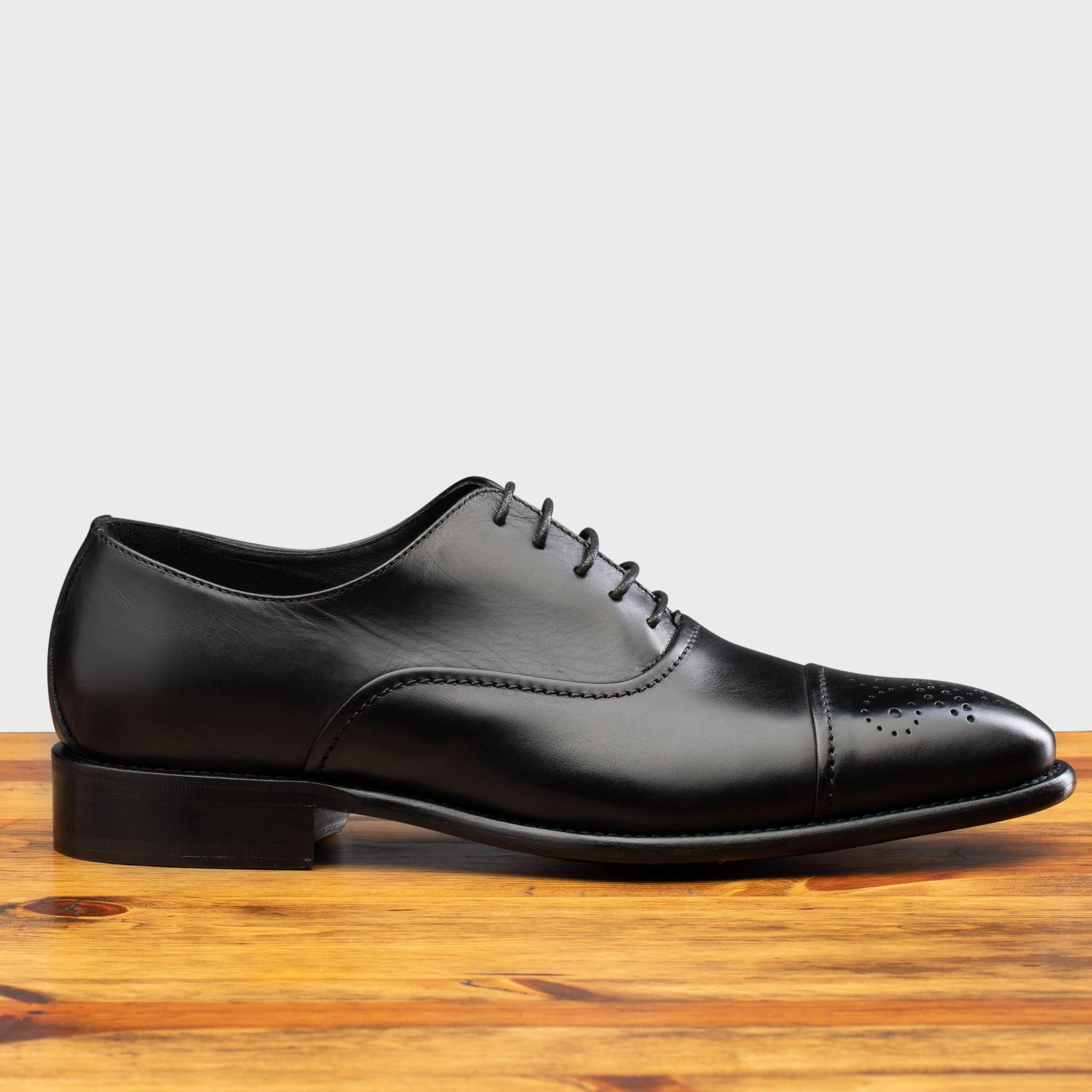 Side profile of the 2361 Calzoleria Toscana Black Cayenne Calf Cap Toe on top of  a wooden table