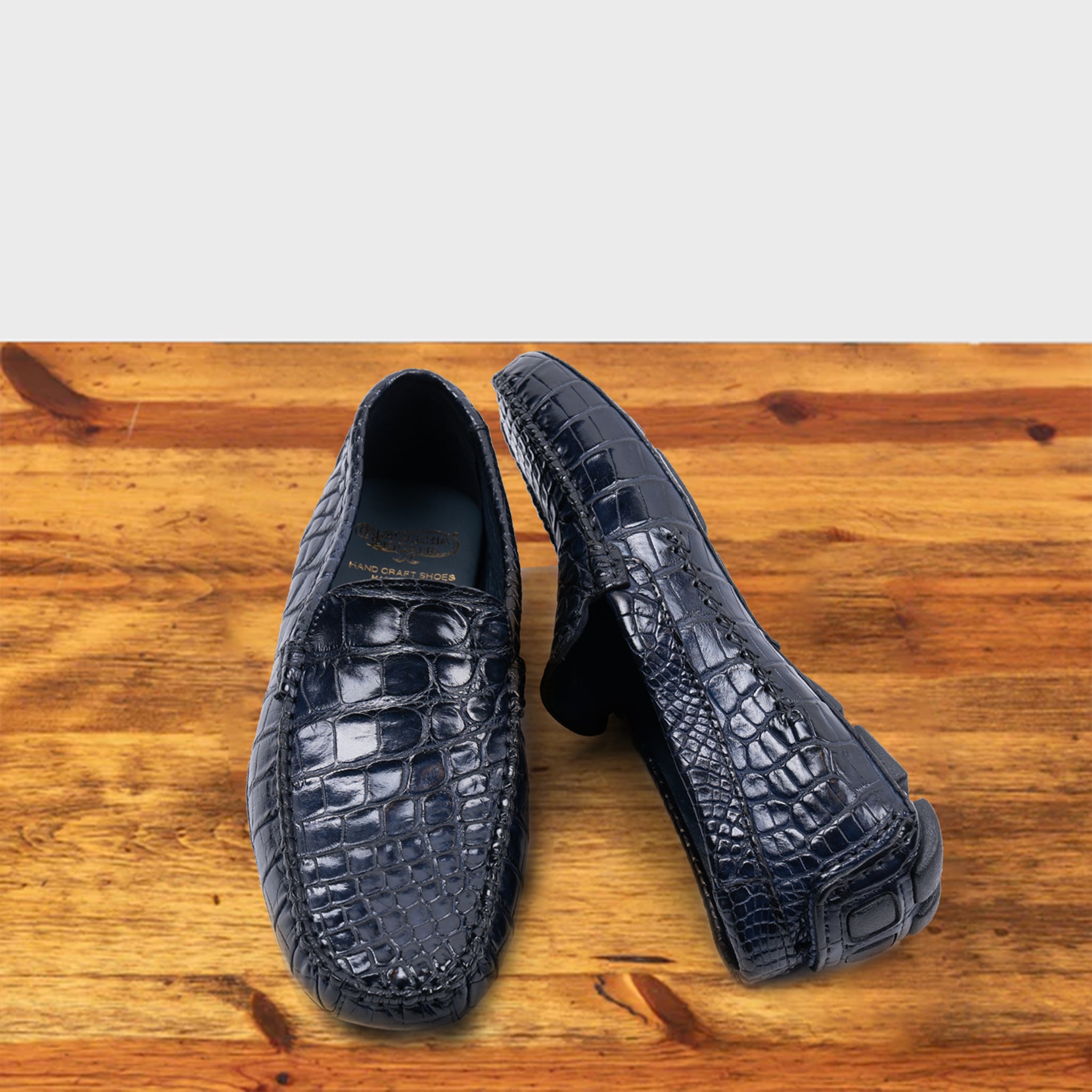 A Pair of Blue crocodile-patterned loafer on a wooden surface with a light gray background