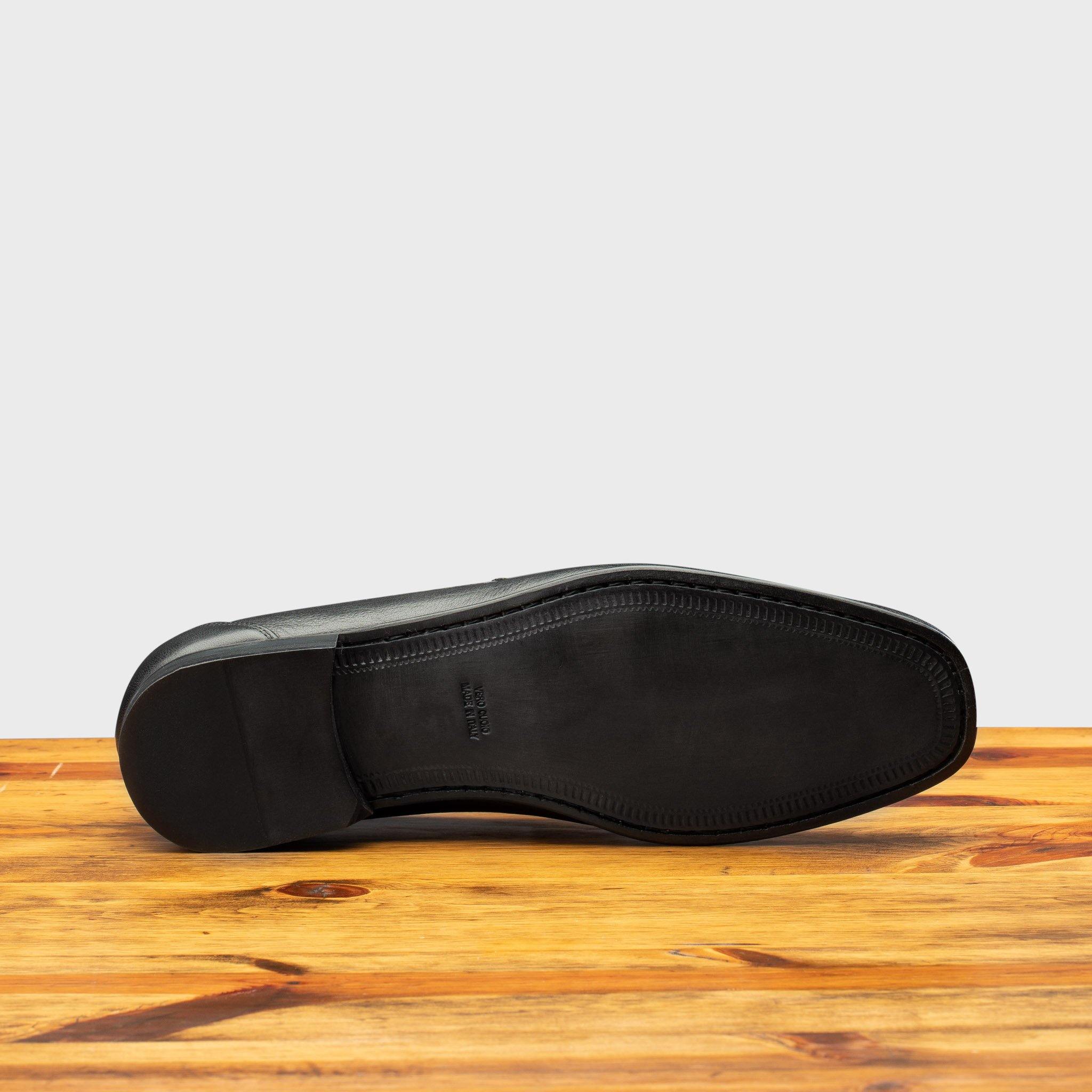 Outsole of Black loafer shoe on a wooden surface with a light gray background