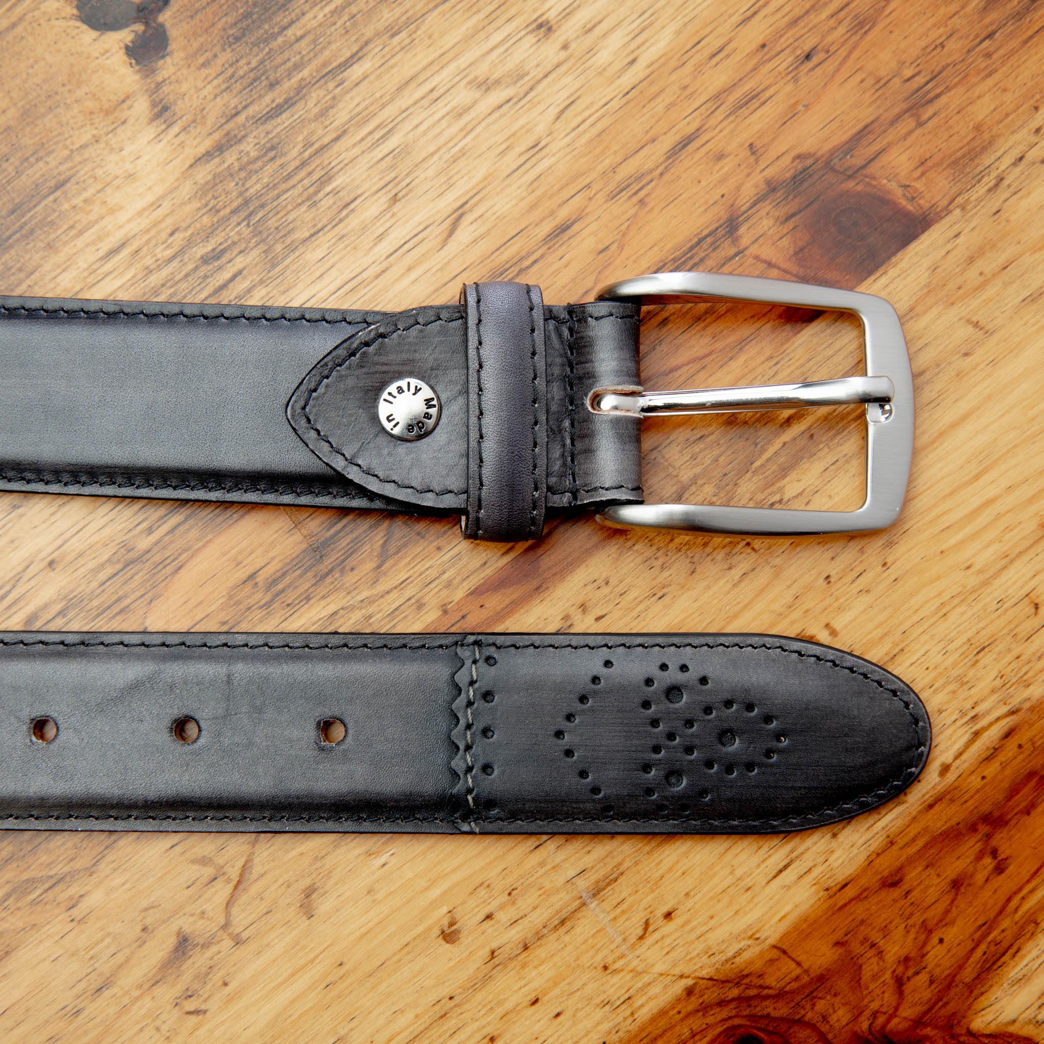 Up close picture of the silver buckle and perforated tip of C5677 Calzoleria Toscana Graphite Artisan Dress Belt on top of a wooden table