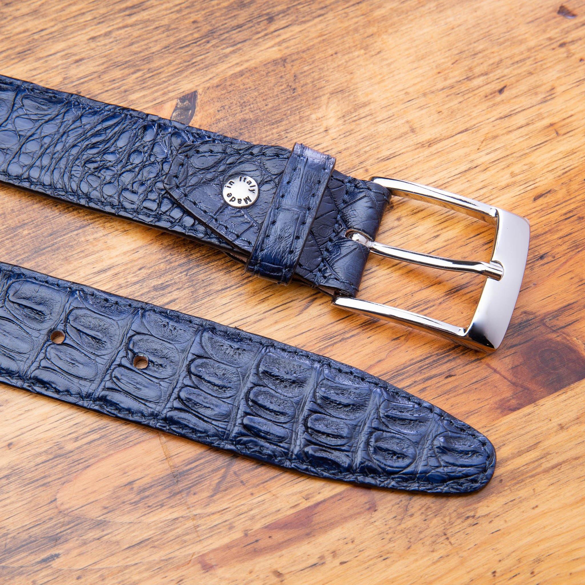 Up close picture of the silver buckle of C7981 Calzoleria Toscana Navy Exotic Hornback Belt on top of a wooden table