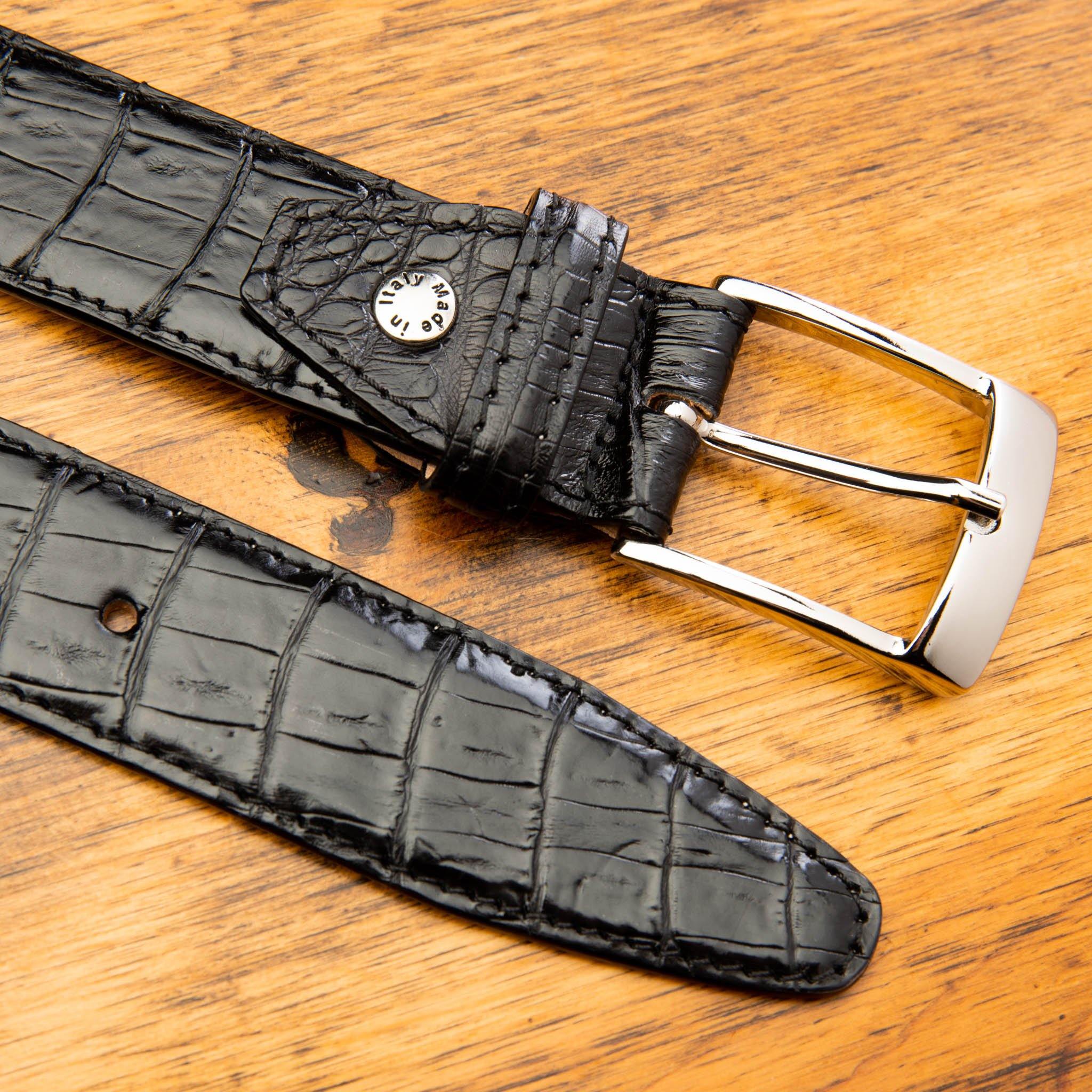 Up close picture of the silver buckle of C7981 Calzoleria Toscana Black Exotic Hornback Belt on top of a wooden table