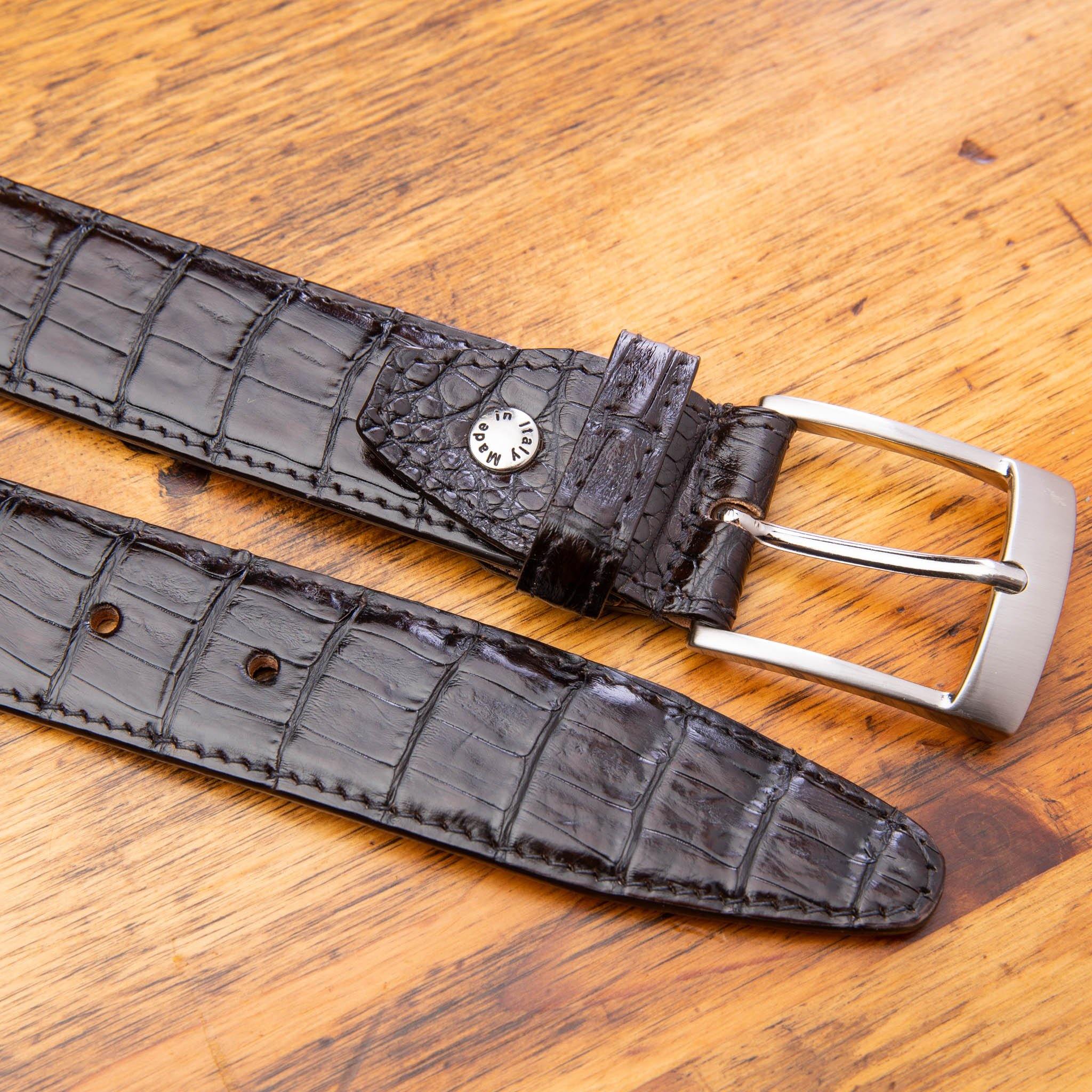 Up close picture of  the silver buckle of C7981 Calzoleria Toscana Dark Brown Exotic Hornback Belt on top of a wooden table