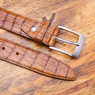 Up close picture of the silver buckle of C7981 Calzoleria Toscana Brick Exotic Hornback Belt on top of a wooden table