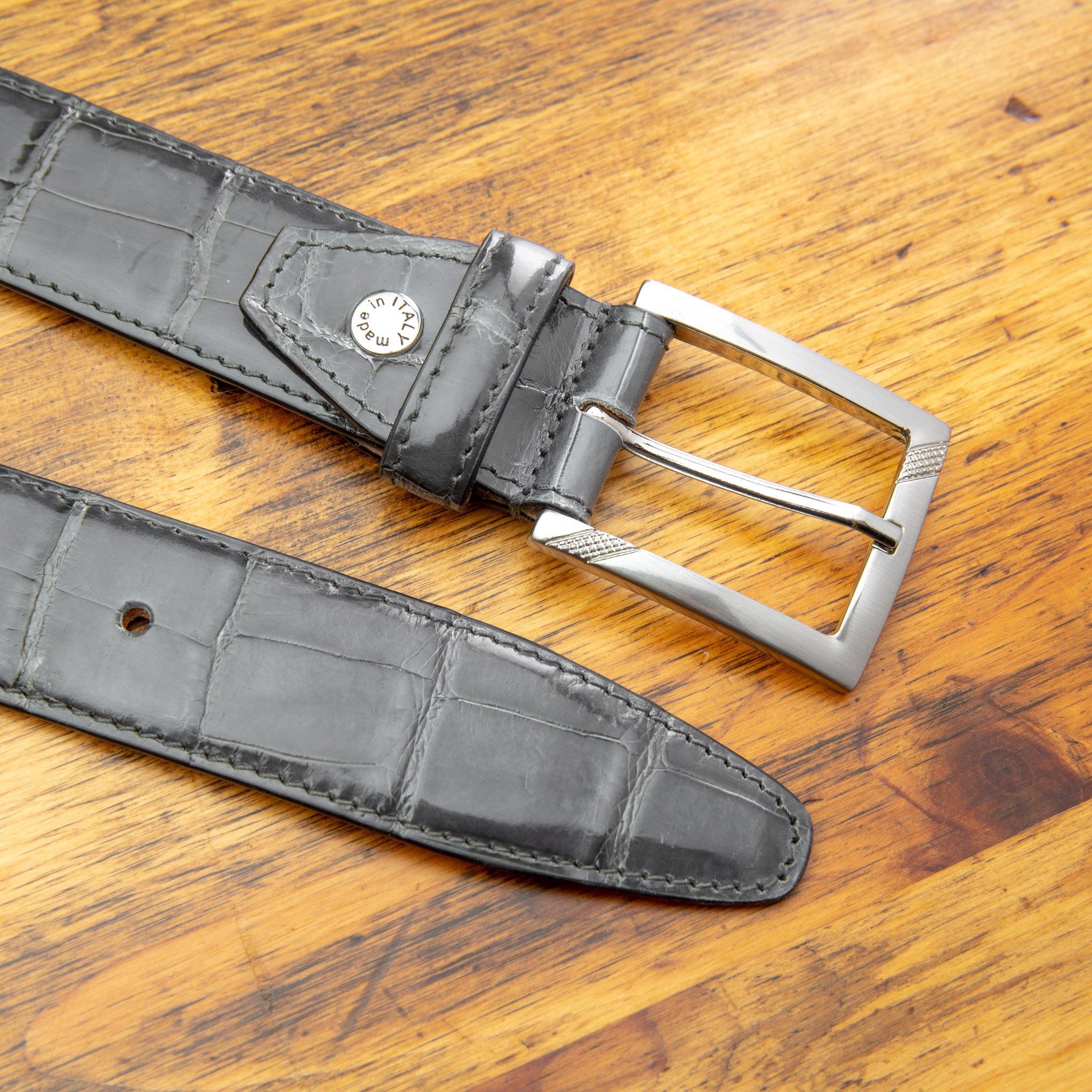 Up close picture of the silver buckle of C8099 Calzoleria Toscana Gray Crocodile Belt on top of a wooden table