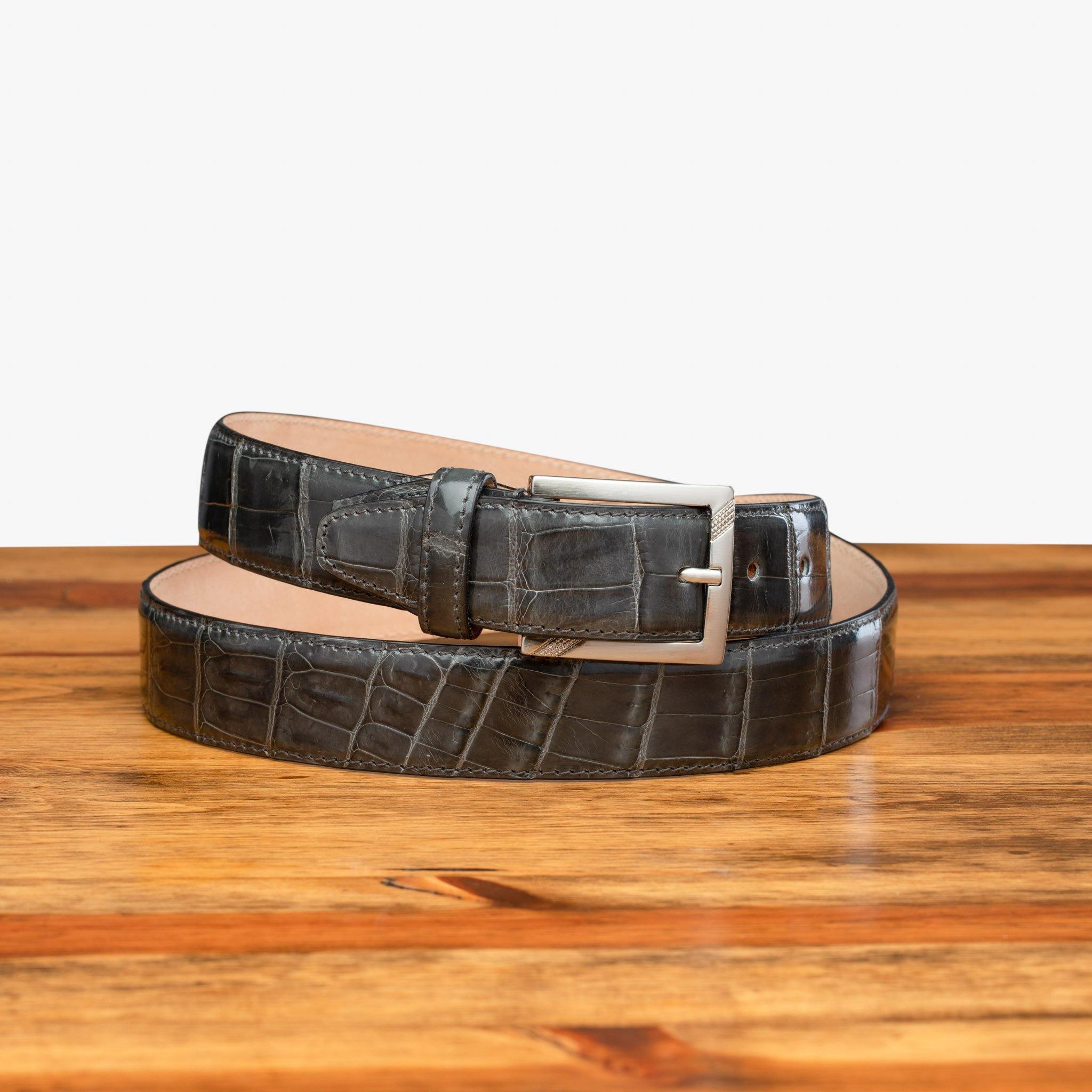 Front profile of C8099 Calzoleria Toscana Gray Crocodile Belt curled up on top of a wooden table