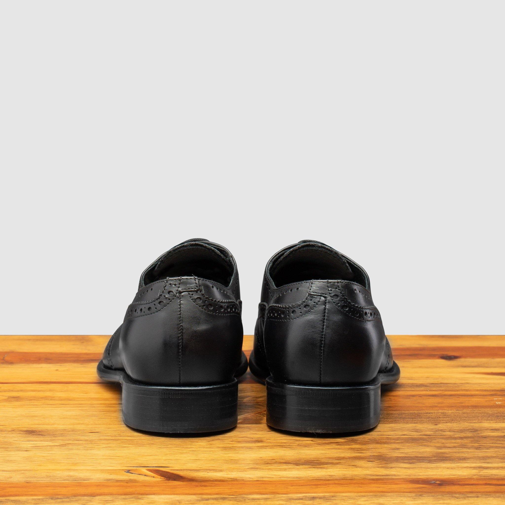 Back View of black leather dress shoe on a wooden surface with a light gray background