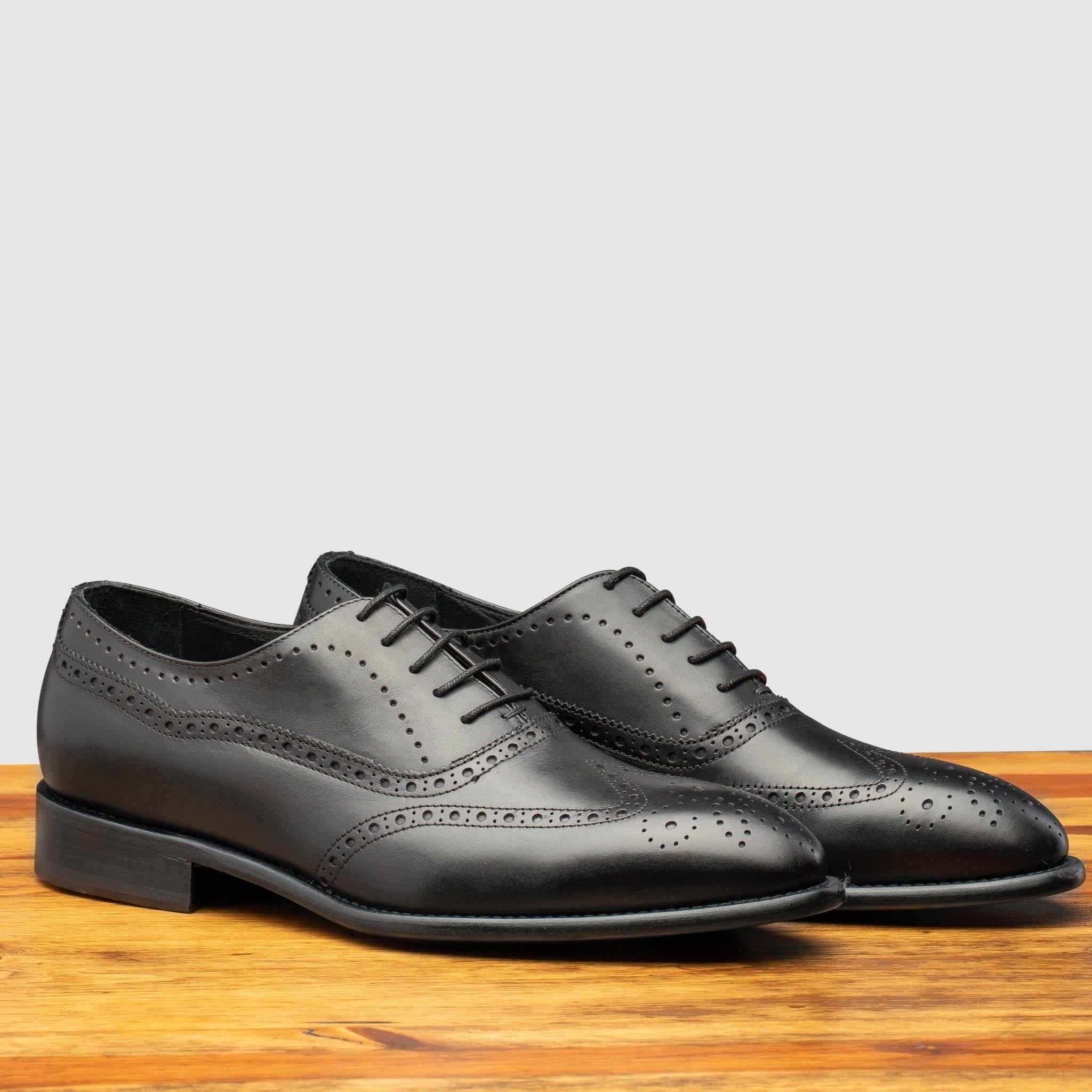 Pair of black leather dress shoe on a wooden surface with a light gray background