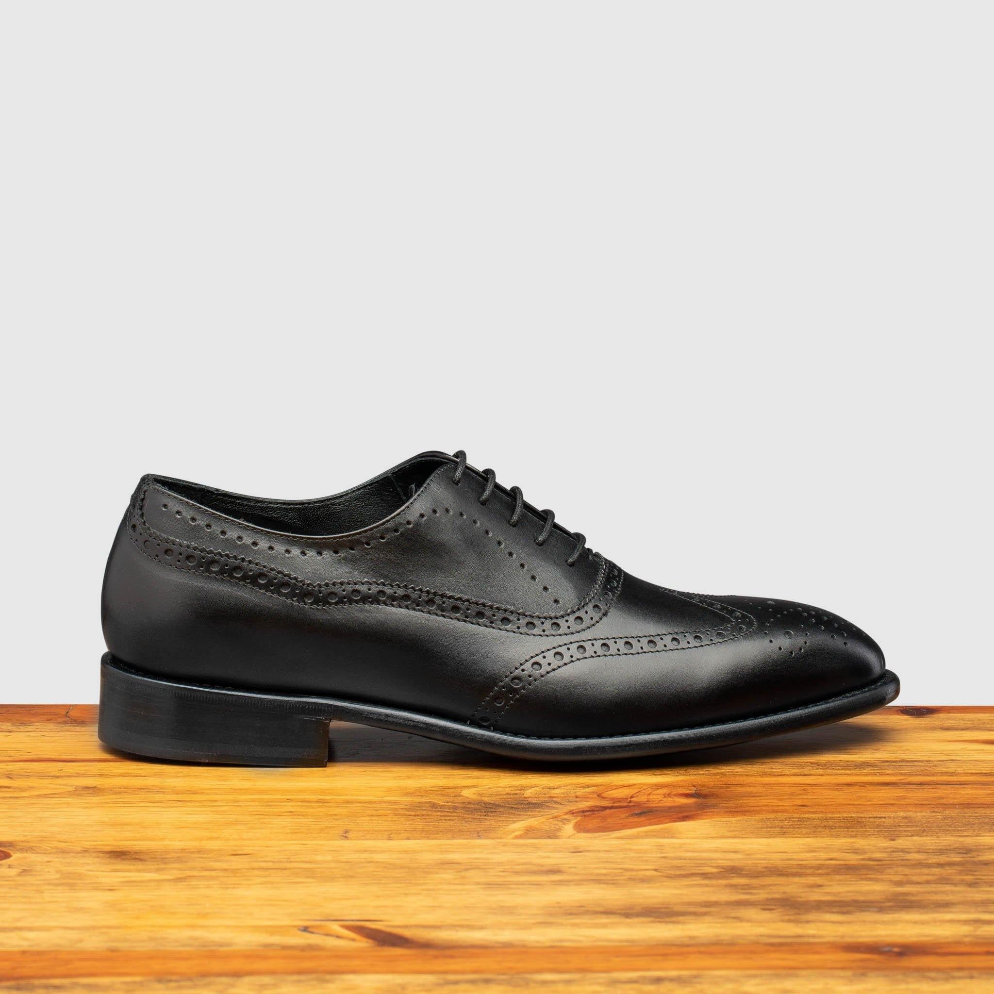 Black leather dress shoe on a wooden surface with a light gray background