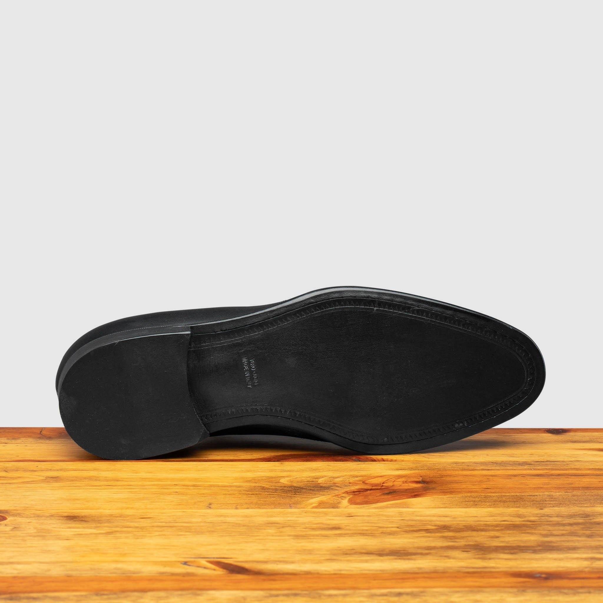 Outsole of black leather dress shoe on a wooden surface with a light gray background