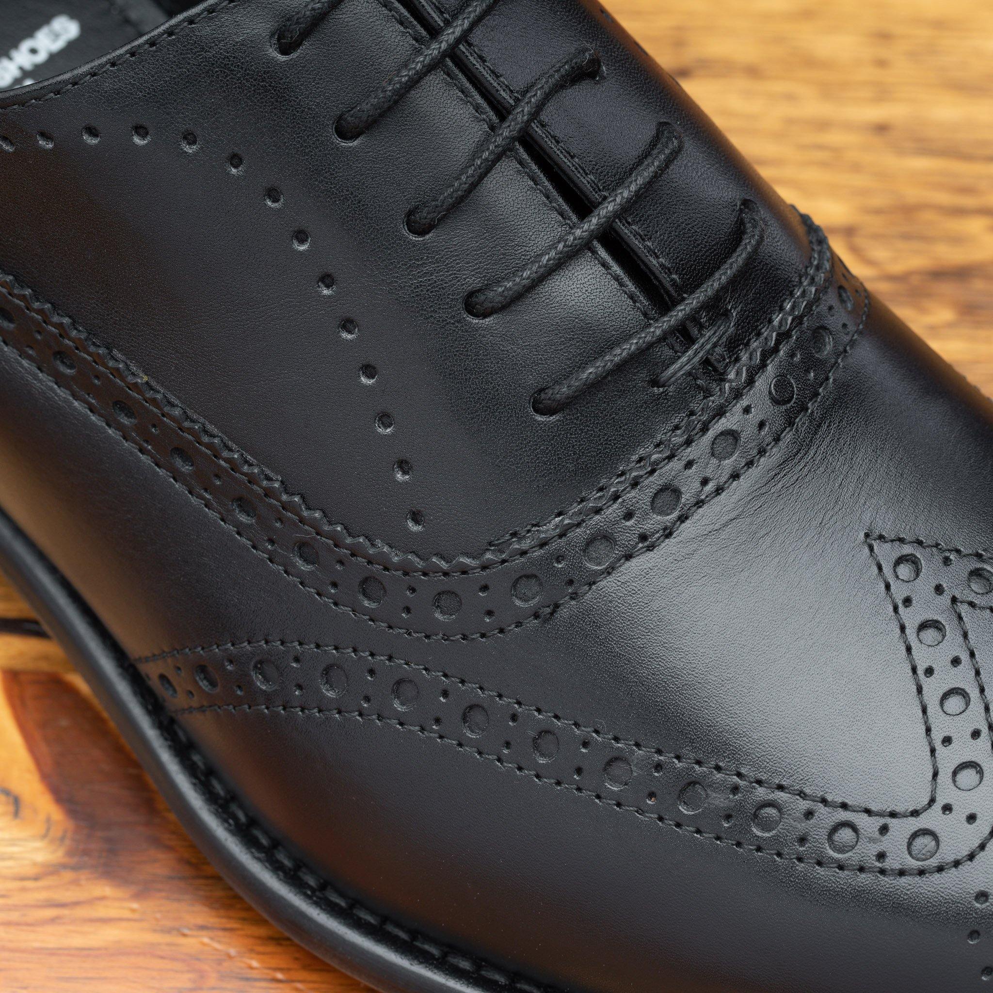 Close view of black leather dress shoe on a wooden surface