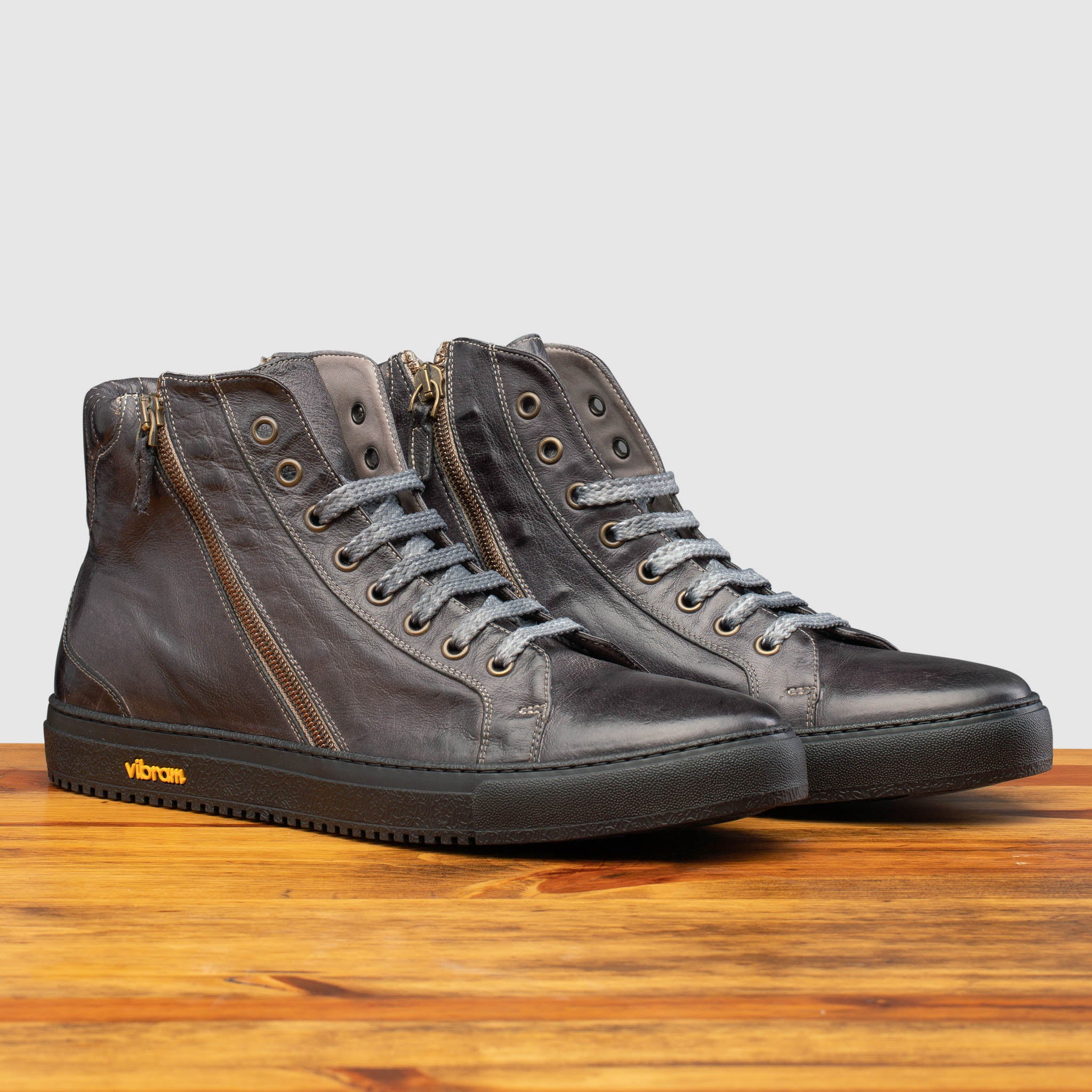 Pair of Q555 Stone Calzoleria Toscana Stone Dip-Dyed Buff Calf High Top on top of a wooden table