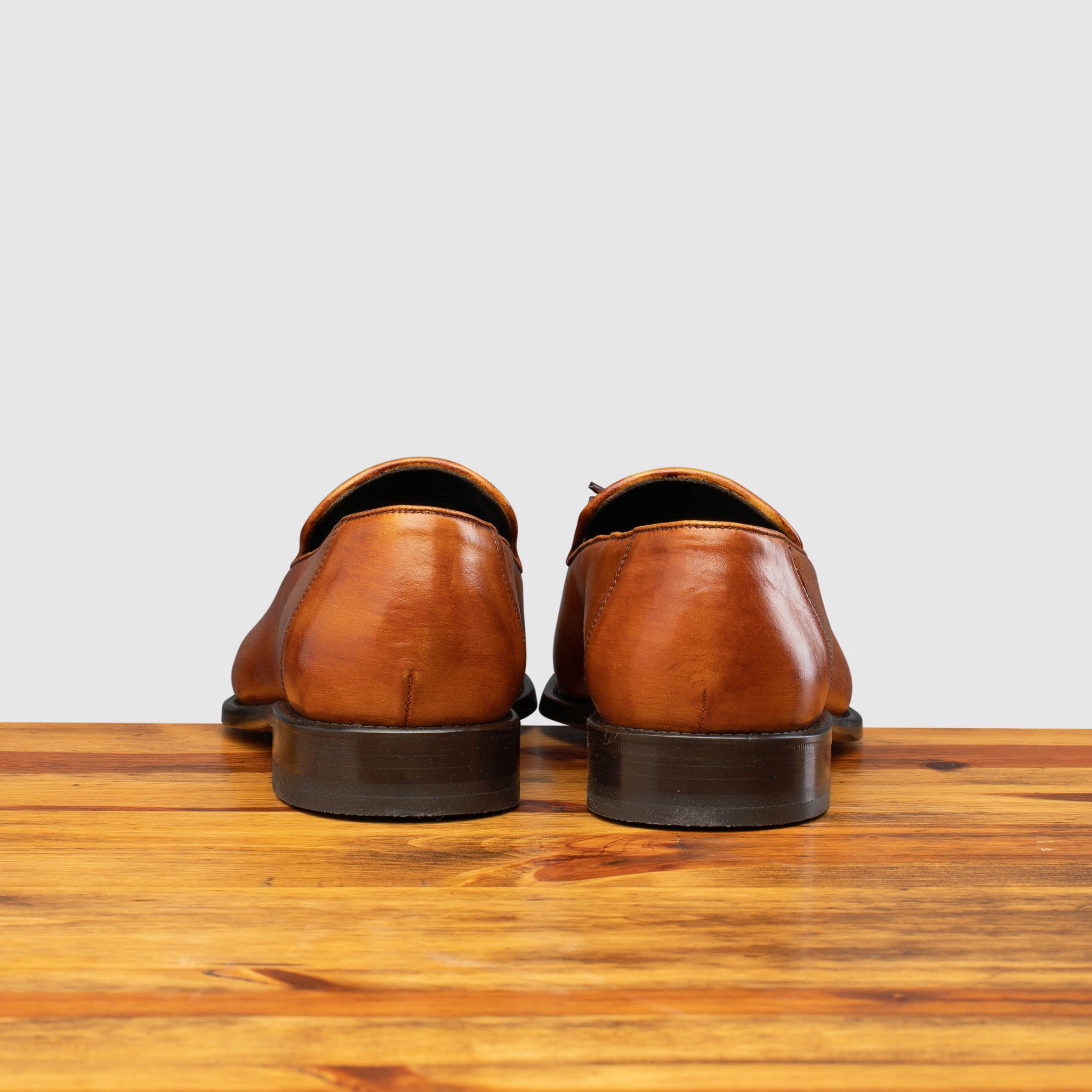 Back view of Caramel leather loafer with a tassel on a wooden surface