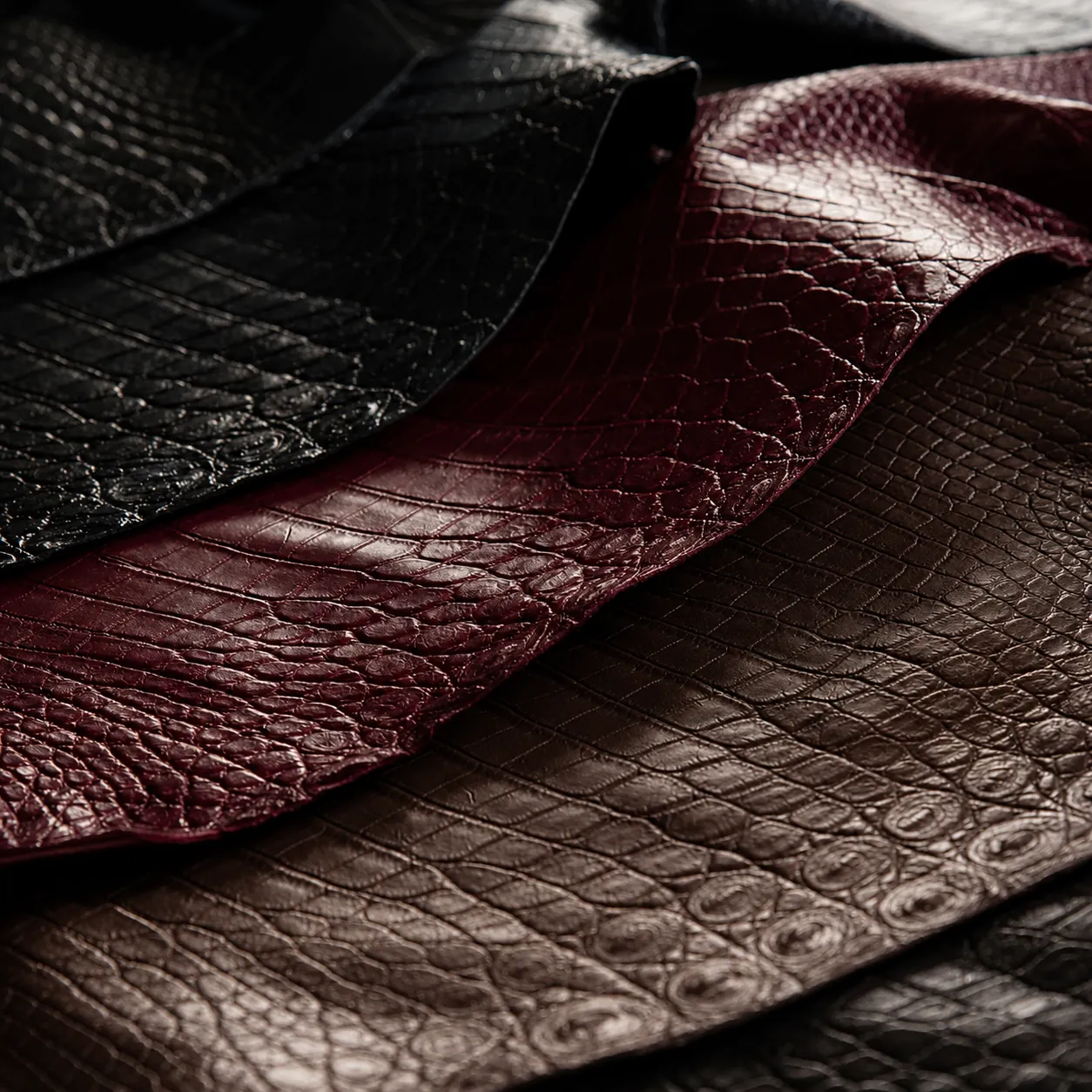 A piece of polished black Nile crocodile leather draped over an edge, showing its natural fold and glossy tile pattern.