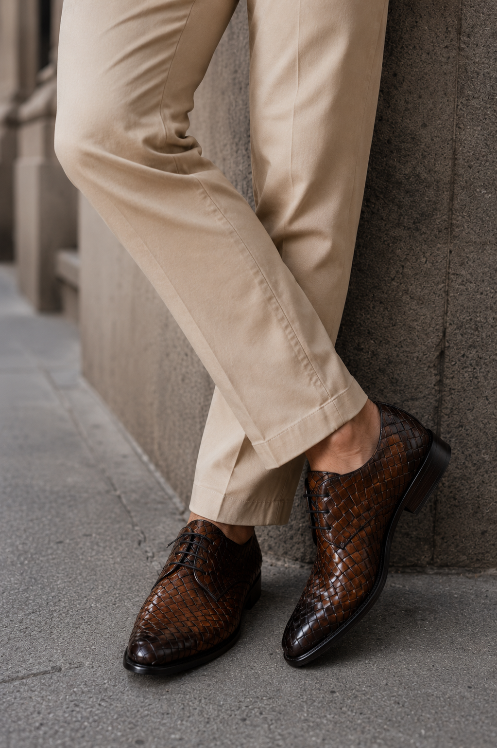 Handcrafted mahogany handwoven intrecciato Italian leather Gallo lace-ups by Calzoleria Toscana, styled with cream trousers against a stone wall.