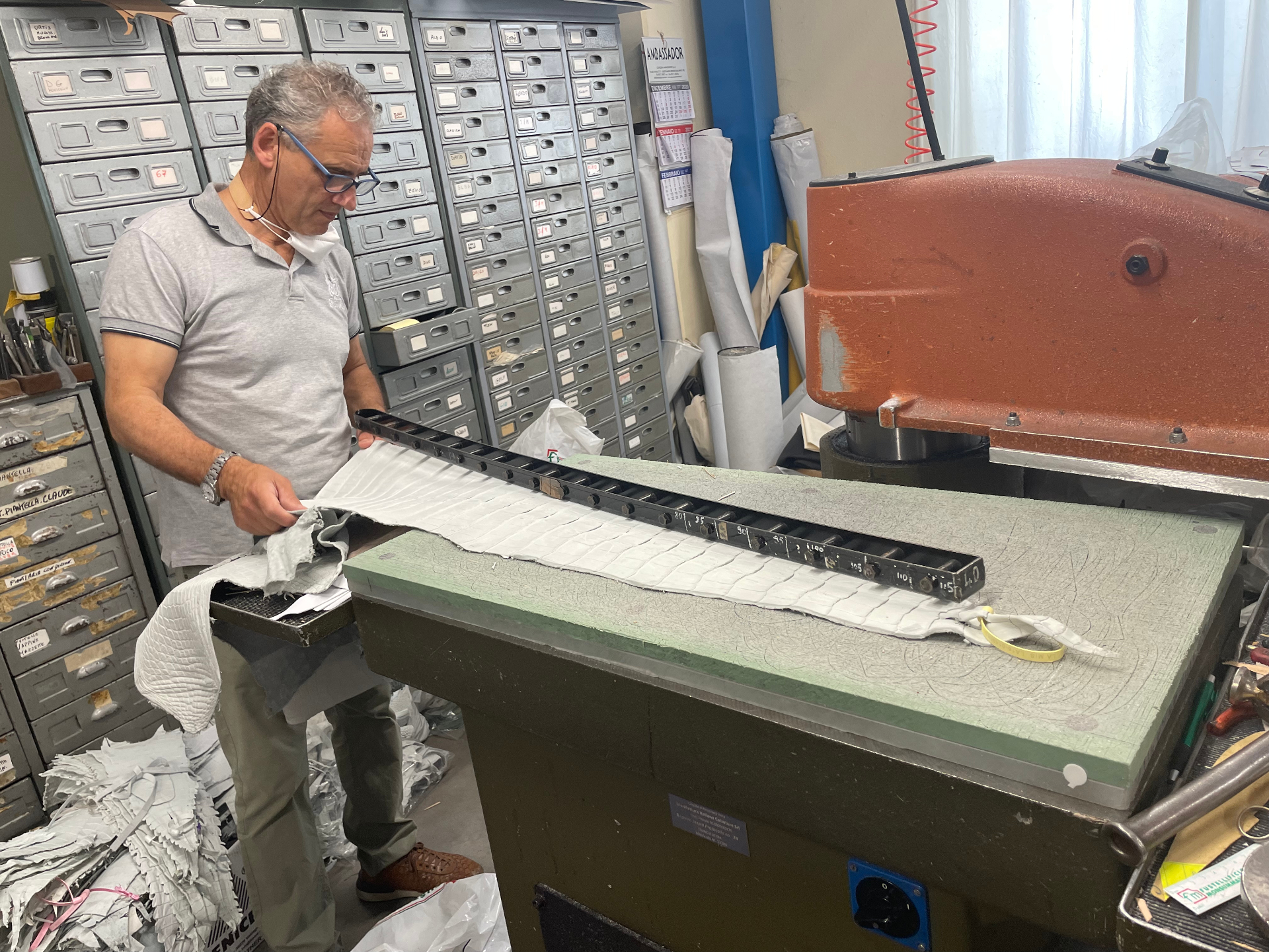 A master artisan hand-placing a steel die on a panel of crocodile leather before cutting