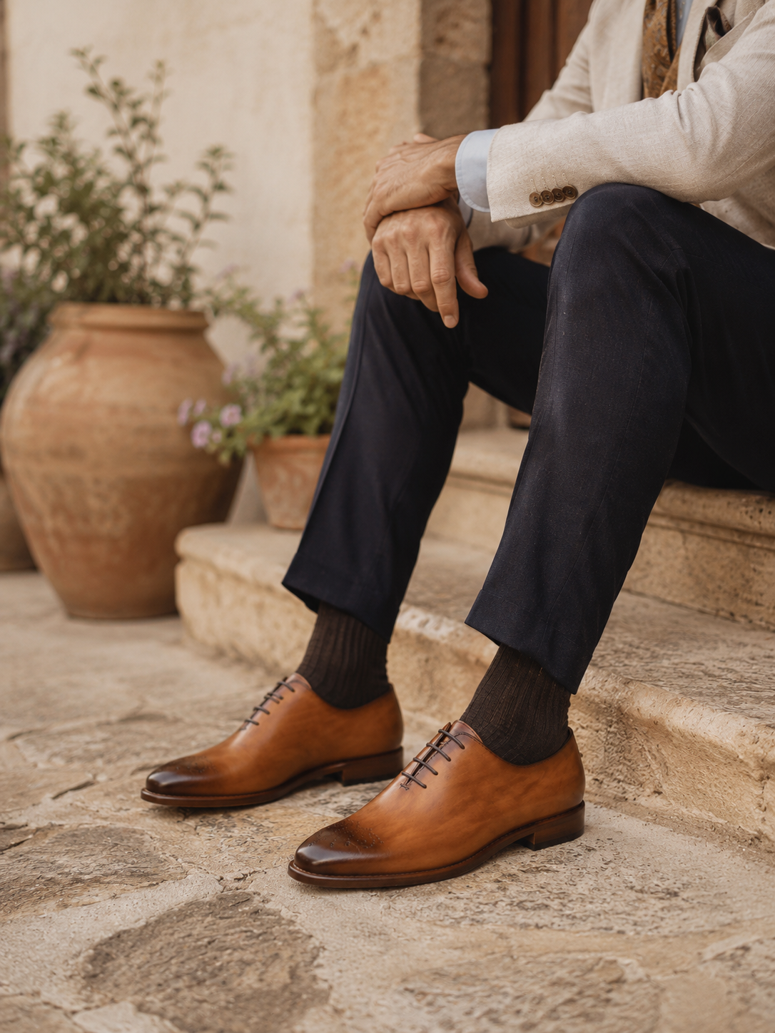 A gentleman seated on Mediterranean stone steps wearing cognac hand-painted Calzoleria Toscana dress shoes with navy trousers