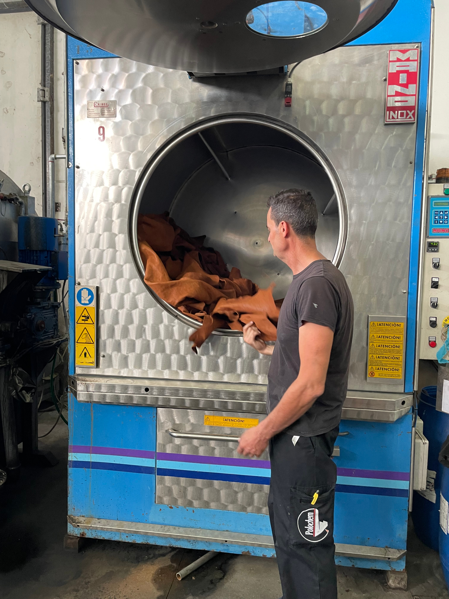 A Tuscan artisan unloading freshly tumbled cognac-colored leather hides from a large softening drum