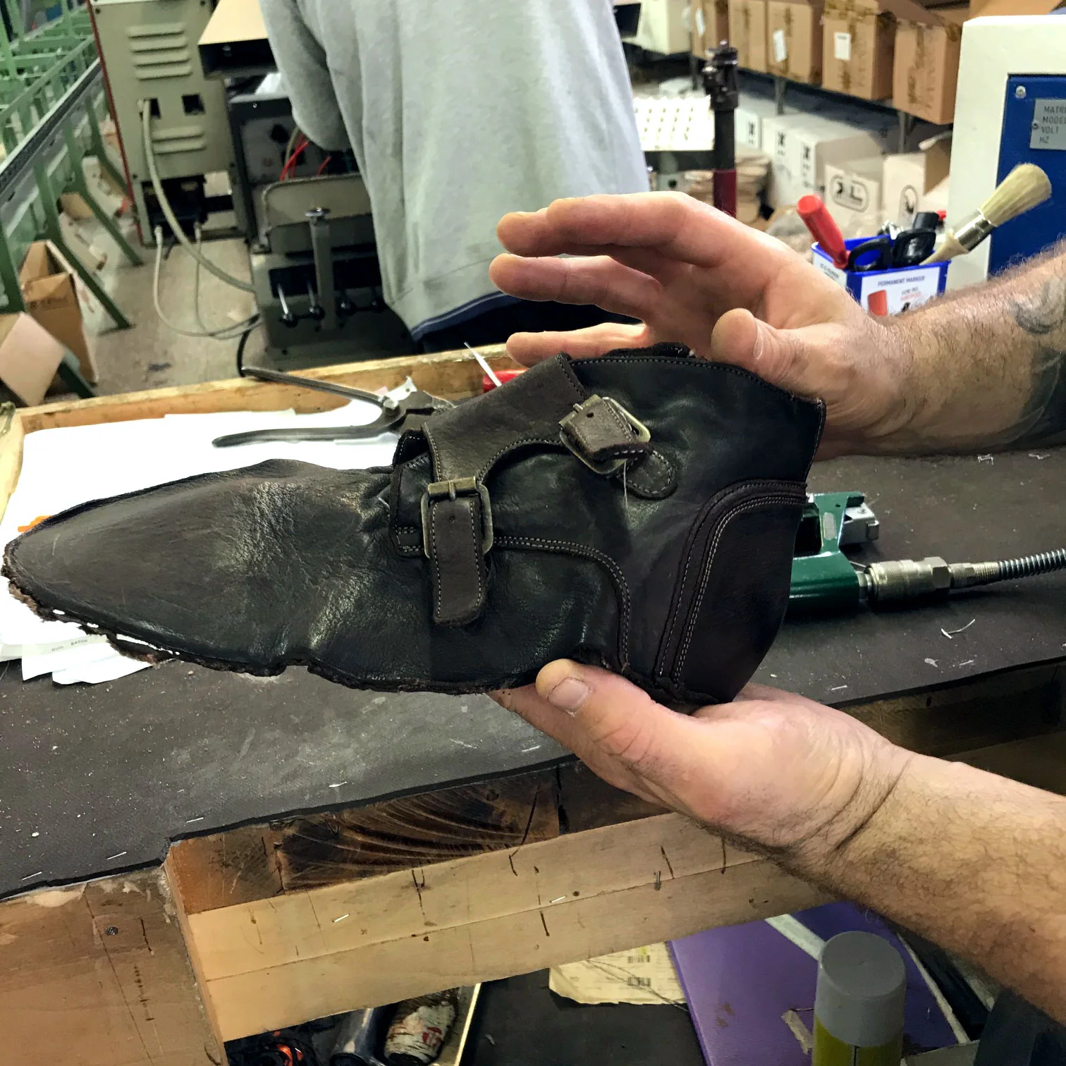 An artisan inspecting a freshly dip-dyed double-monk leather upper on the workshop bench before final finishing
