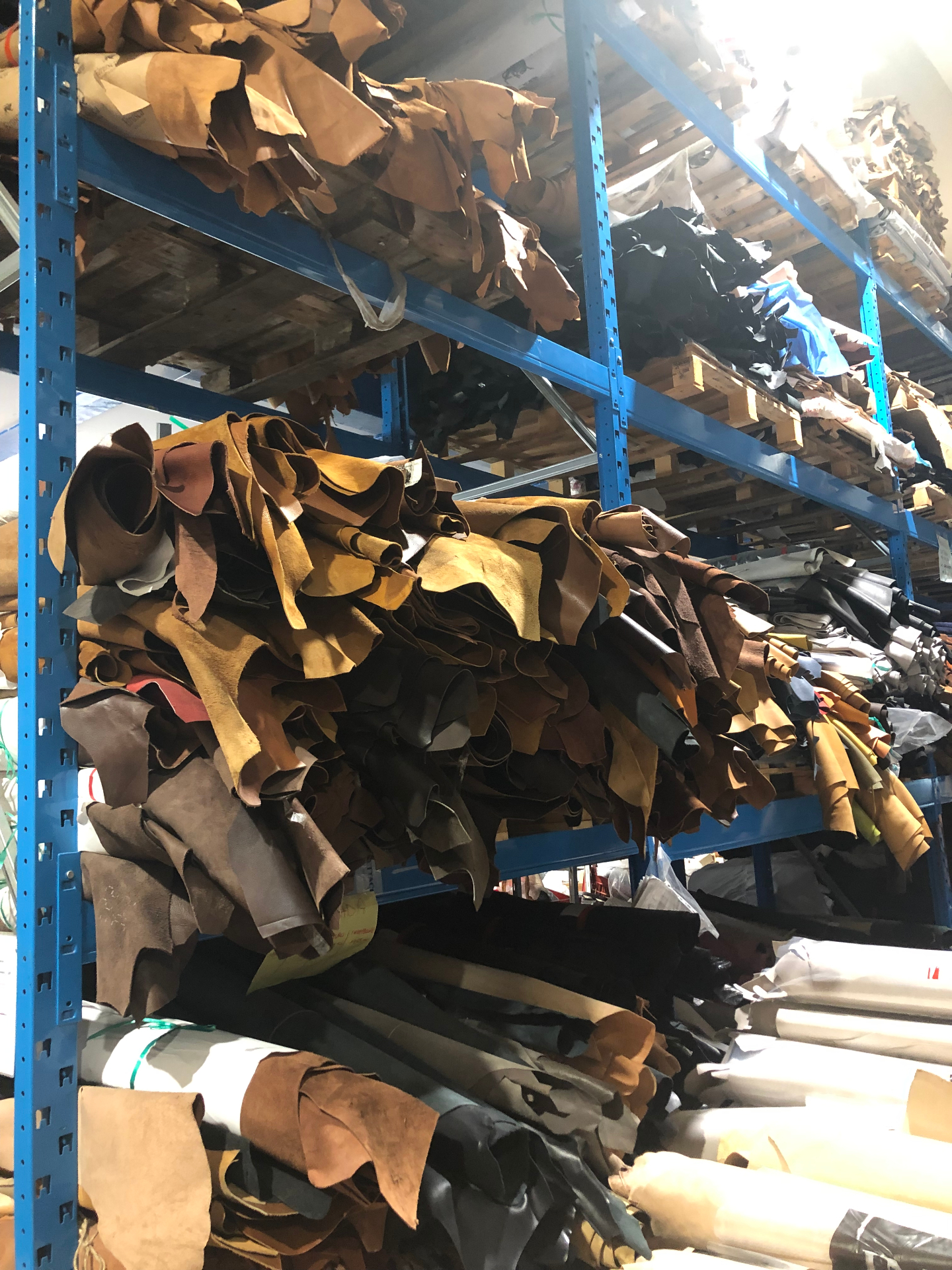Stacks of vegetable-tanned leather hides in cognac, tobacco, and walnut tones on warehouse racks, ready for hand selection