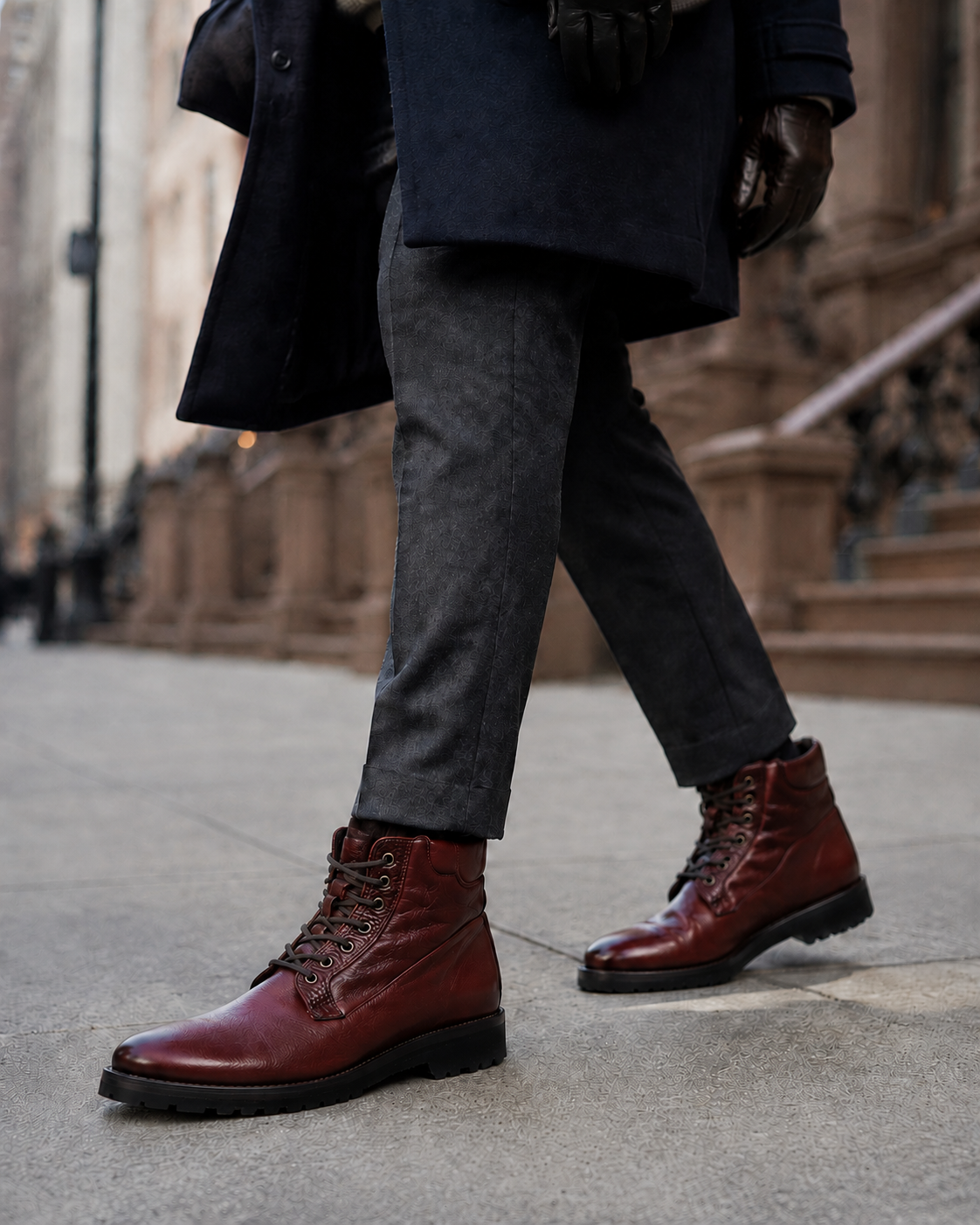 Man in a navy overcoat, charcoal trousers and leather gloves walking a city sidewalk, wearing handcrafted burgundy Calzoleria Toscana 3236 shearling-lined lace-up boots.