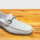 White loafer shoe with silver buckle on a wooden surface